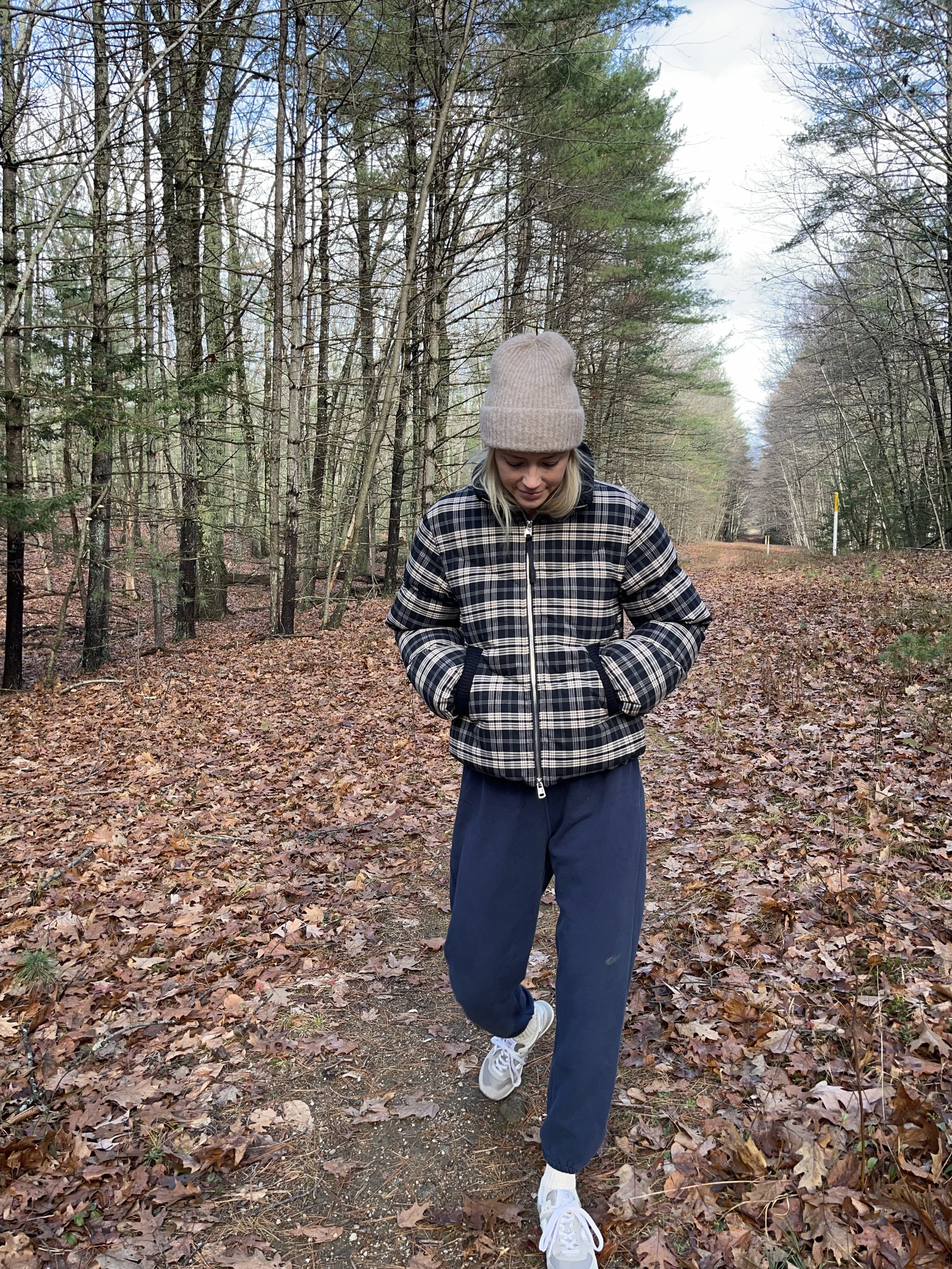 A woman taking a mirror selfie in a spacious, well-lit living room with hardwood floors, large windows, a white sofa, and a side table with a plant.