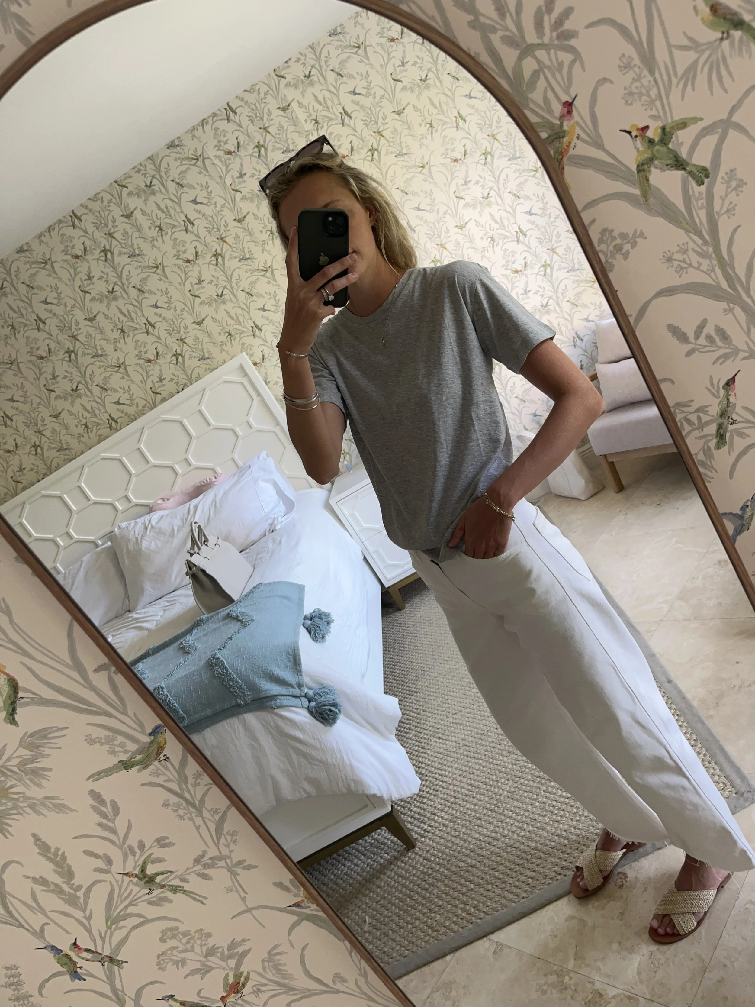 Person taking a mirror selfie in a room with wooden floors, wearing a striped brown and white long-sleeve shirt, light blue jeans, and black and white sneakers.