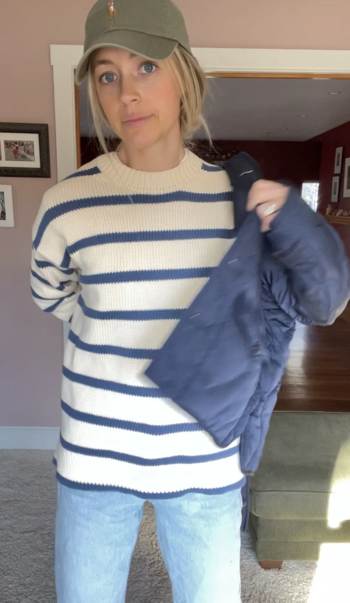 Person taking a mirror selfie in a room with wooden floors, wearing a striped brown and white long-sleeve shirt, light blue jeans, and black and white sneakers.