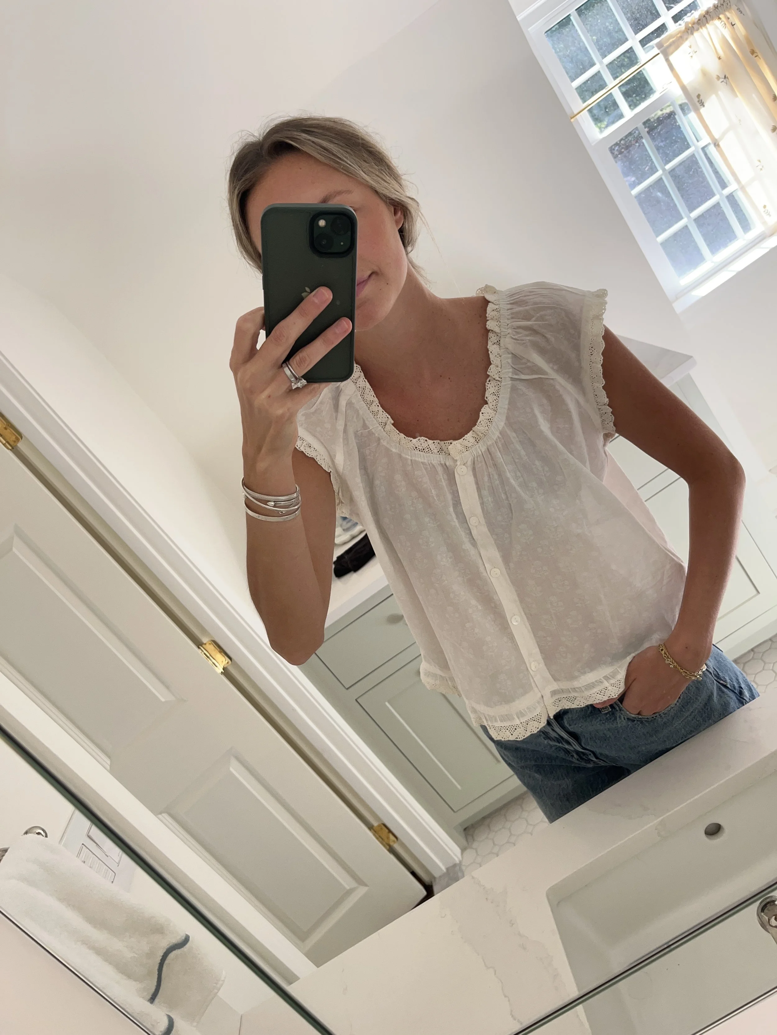 Person taking a mirror selfie in a room with wooden floors, wearing a striped brown and white long-sleeve shirt, light blue jeans, and black and white sneakers.