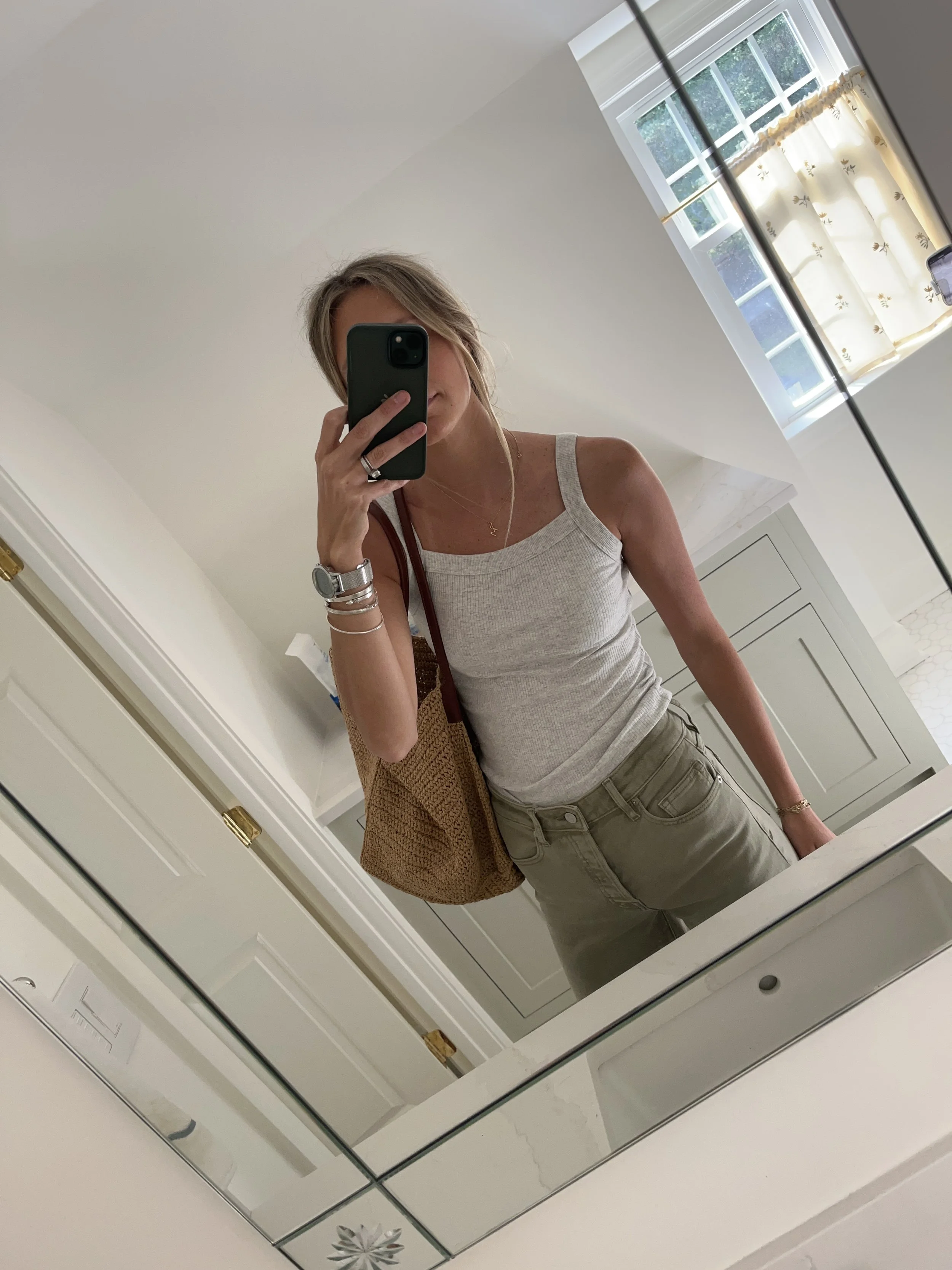 Person taking a mirror selfie in a room with wooden floors, wearing a striped brown and white long-sleeve shirt, light blue jeans, and black and white sneakers.