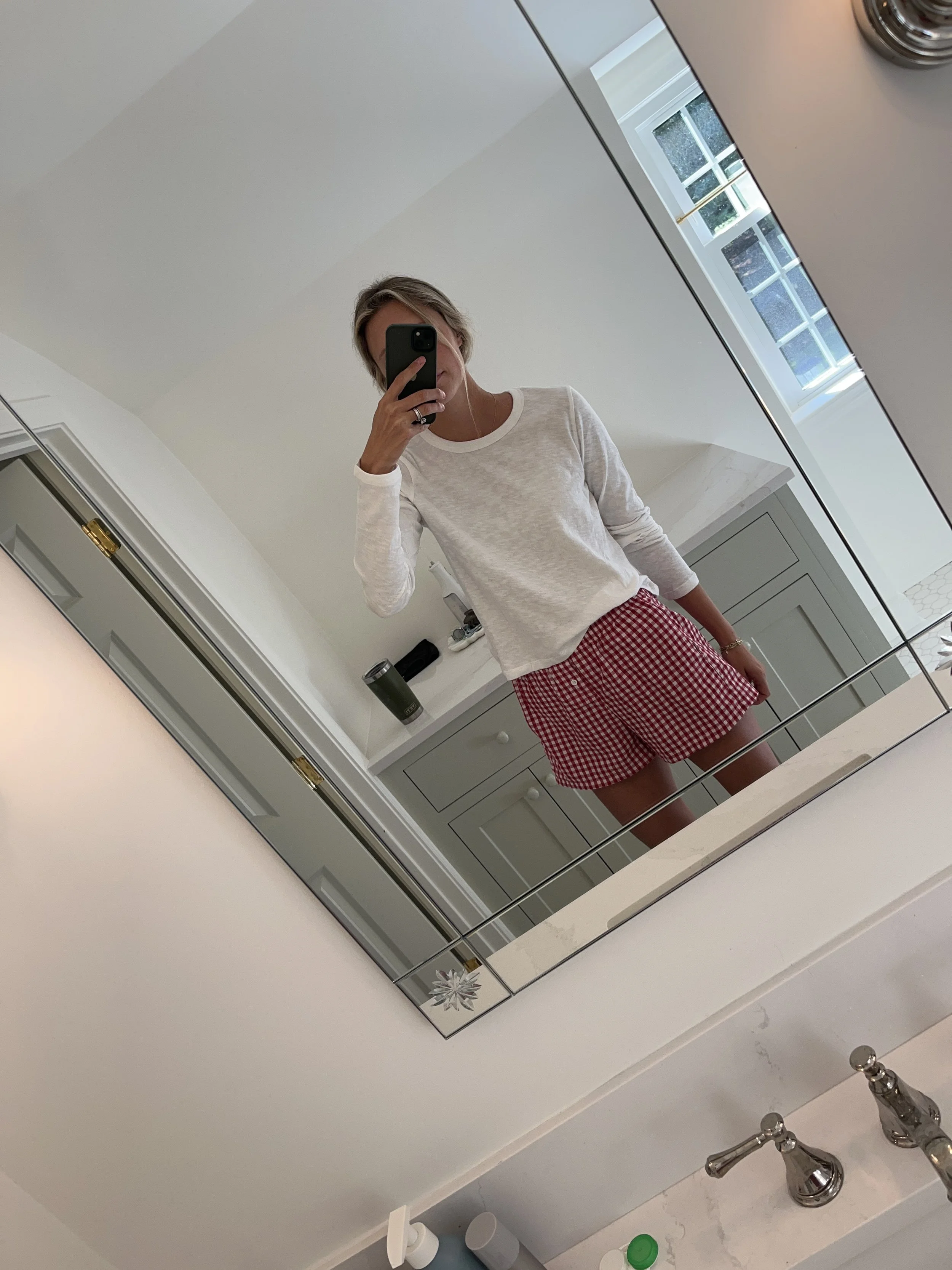 Person taking a mirror selfie in a room with wooden floors, wearing a striped brown and white long-sleeve shirt, light blue jeans, and black and white sneakers.