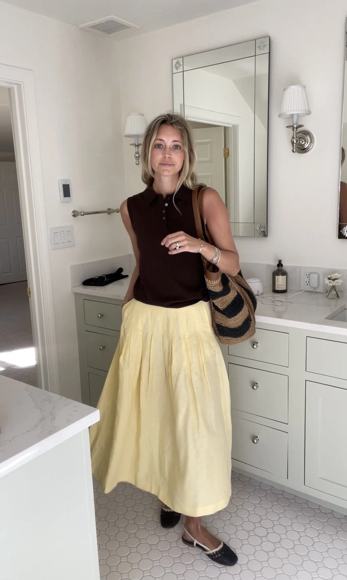 Person taking a mirror selfie in a room with wooden floors, wearing a striped brown and white long-sleeve shirt, light blue jeans, and black and white sneakers.