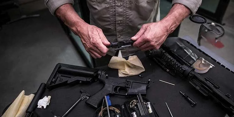 Person cleaning a black firearm with cleaning tools on a black workbench.