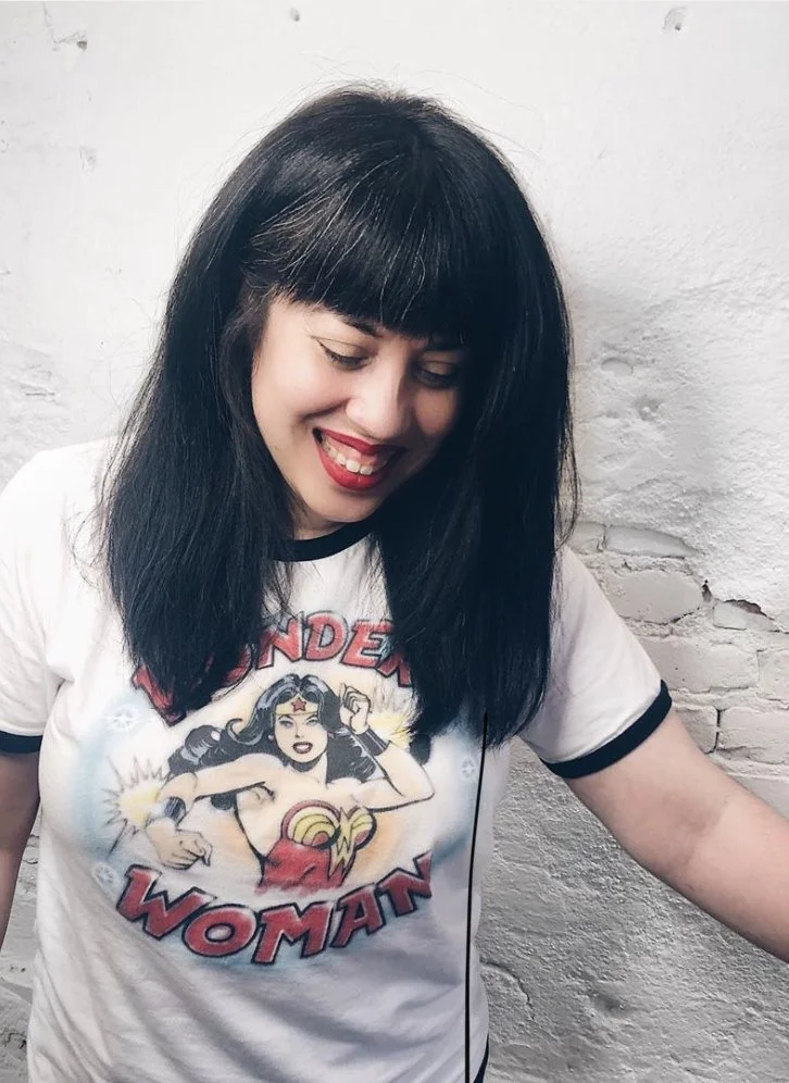 Latina woman with long dark hair smiling wearing wonder woman ringer t-shirt