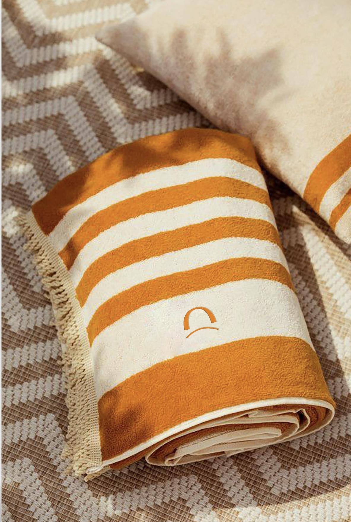 rolled striped orange and white towel on patterned fabric with a beige pillow nearby