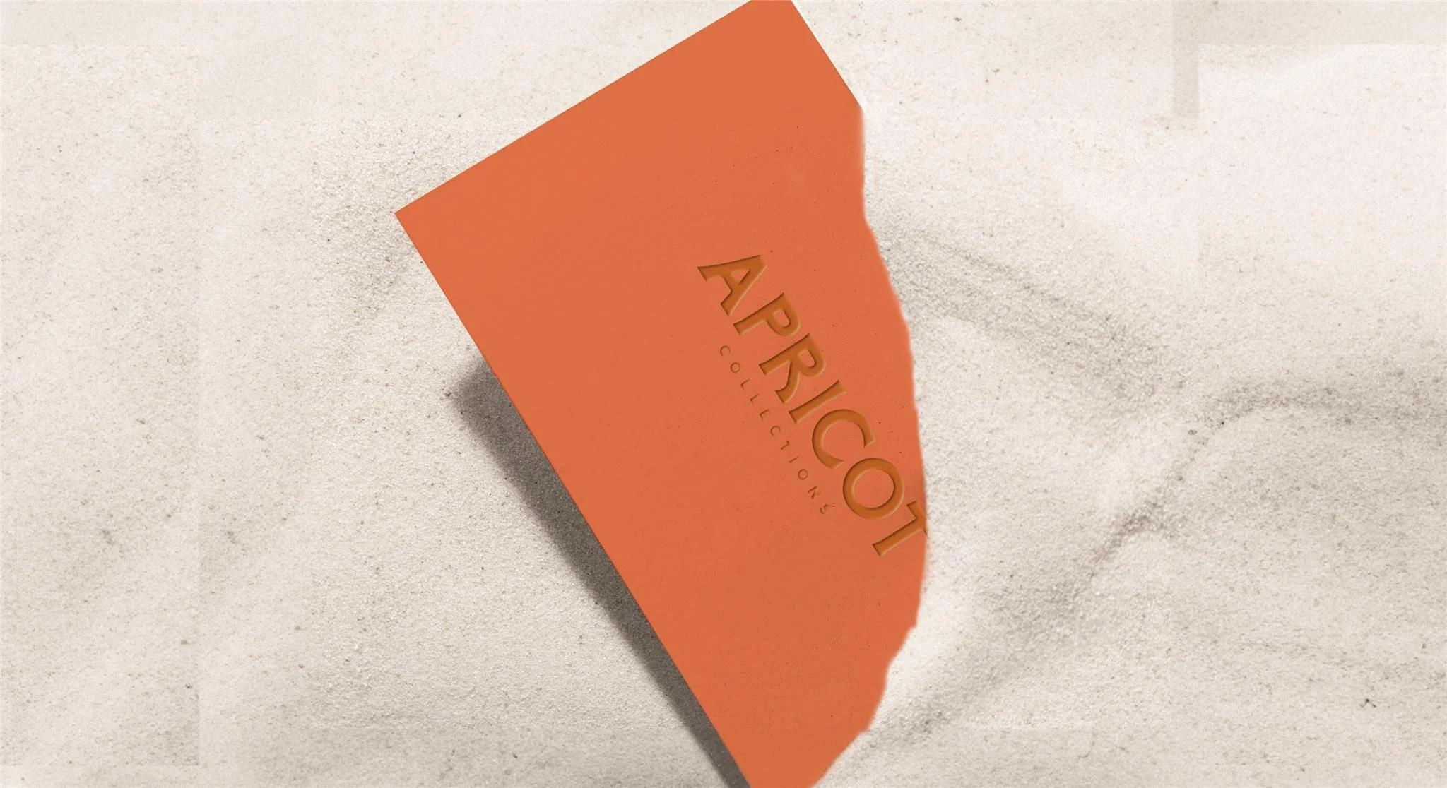 Orange card with the word 'APRICOT' and 'COLLECTIONS' embossed, partially buried in white sand.