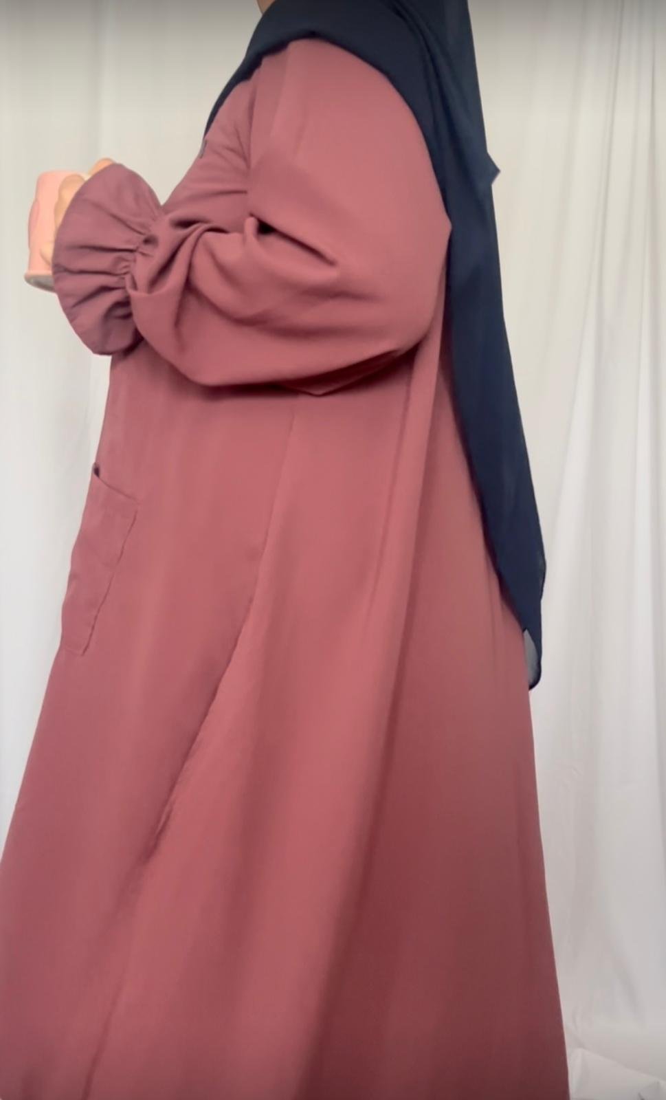 Close-up of a person wearing a pink long tunic and a dark blue headscarf, holding a coffee mug.