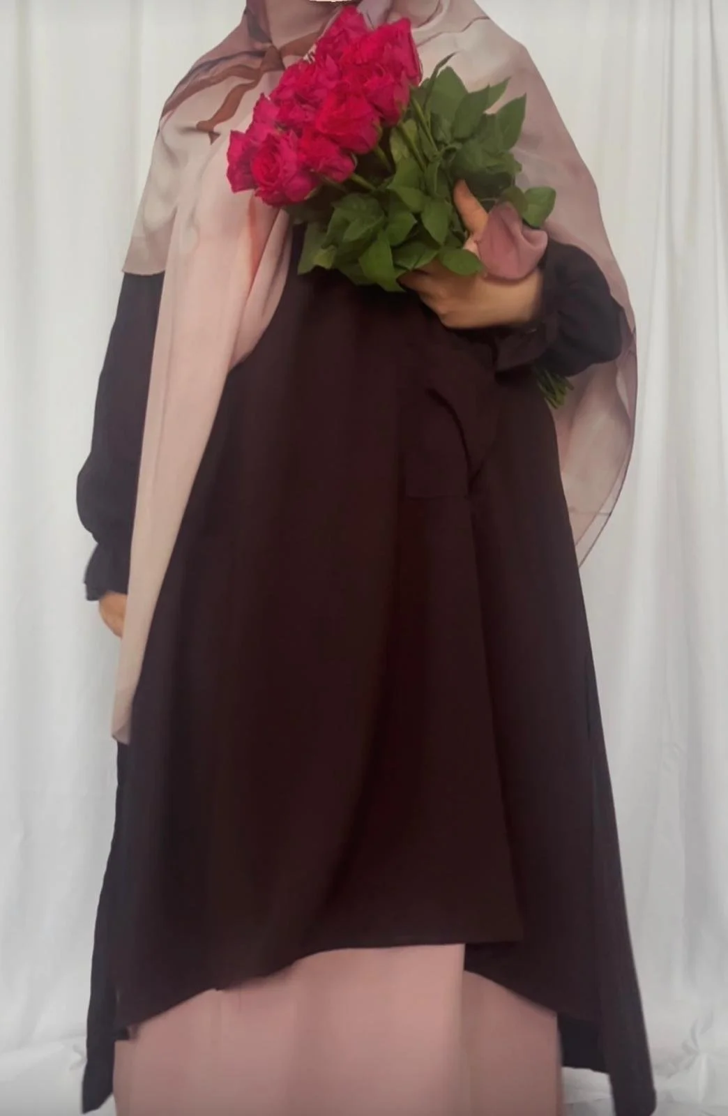 Person holding a bouquet of pink roses in front of a white curtain.