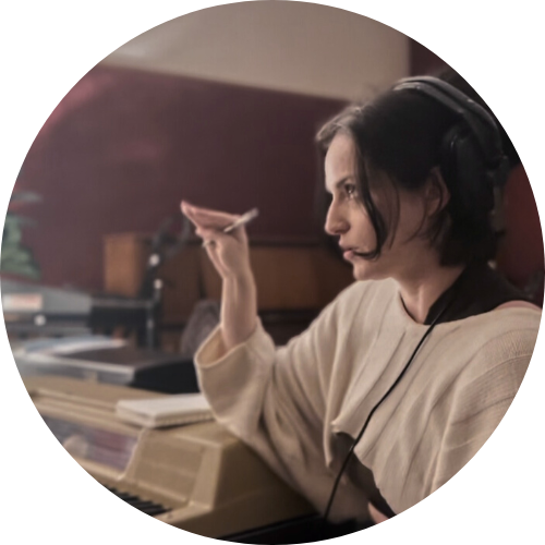 A woman wearing headphones and holding a pen, sitting at a piano with sheet music in front of her.