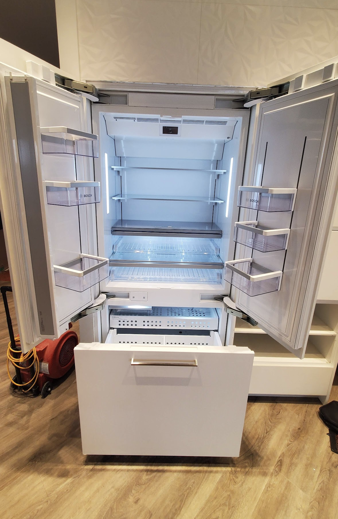 Technician kneeling beside a fridge, checking for a water leak near the bottom.