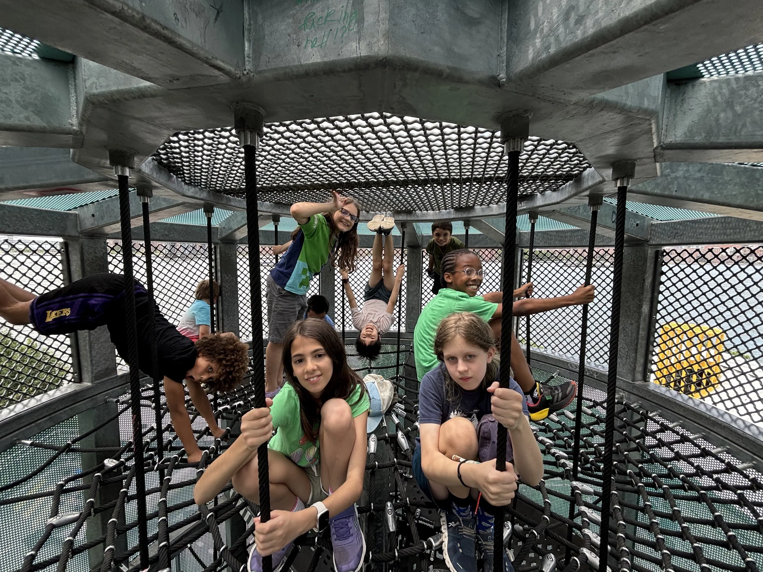 Young children playing and climbing on a netted playground structure, smiling and having fun.