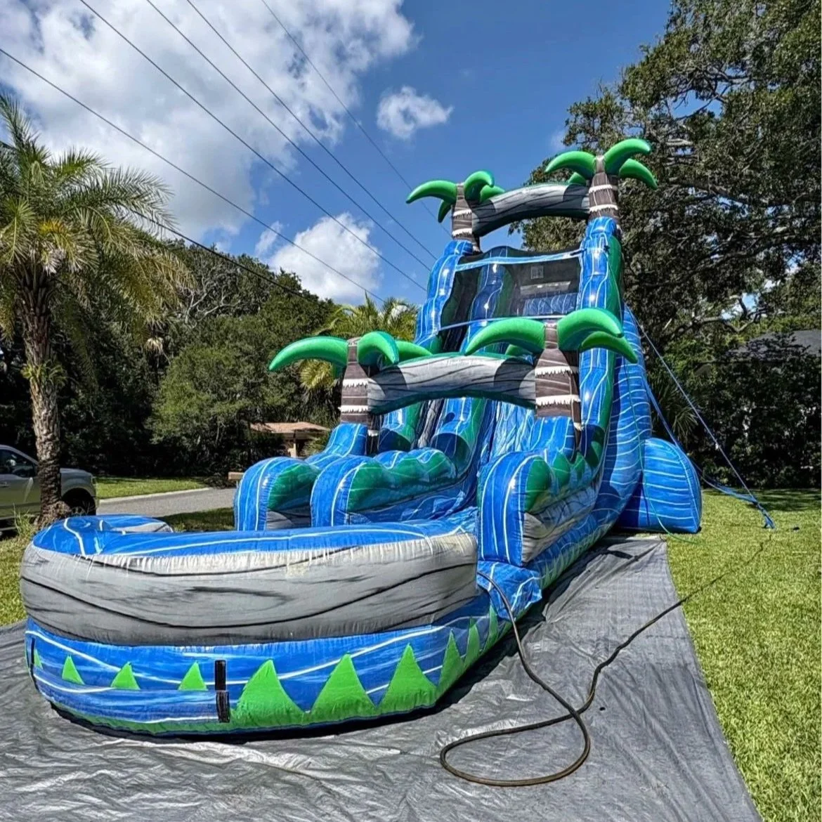 Close-up view of the River Rush inflatable waterslide showing its bold blue color, palm tree accents, and deep splash pool, perfect for large backyard events and birthday parties.