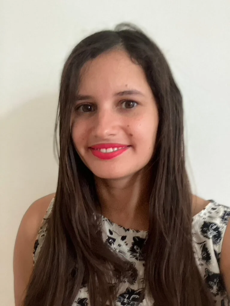 Tori Curbelo, director of education, with long brown hair and light skin, smiling with pink lipstick, wearing a sleeveless top with a black and white animal print, standing against a plain white wall.