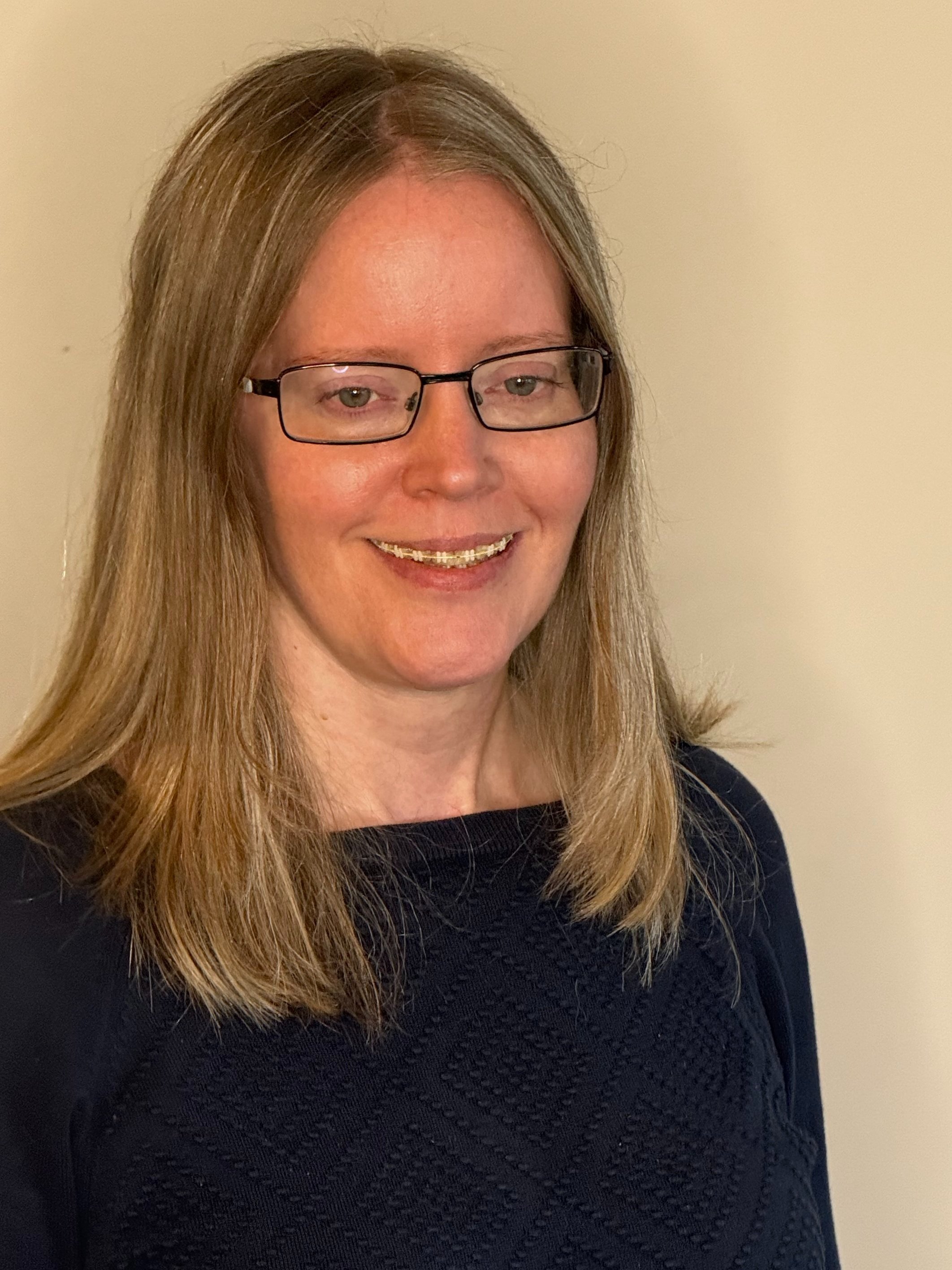 Lindsay Anderson, safe house manager for LifeWay Network, with long, straight blonde hair, glasses, and a black textured sweater, smiling in front of a plain beige wall.