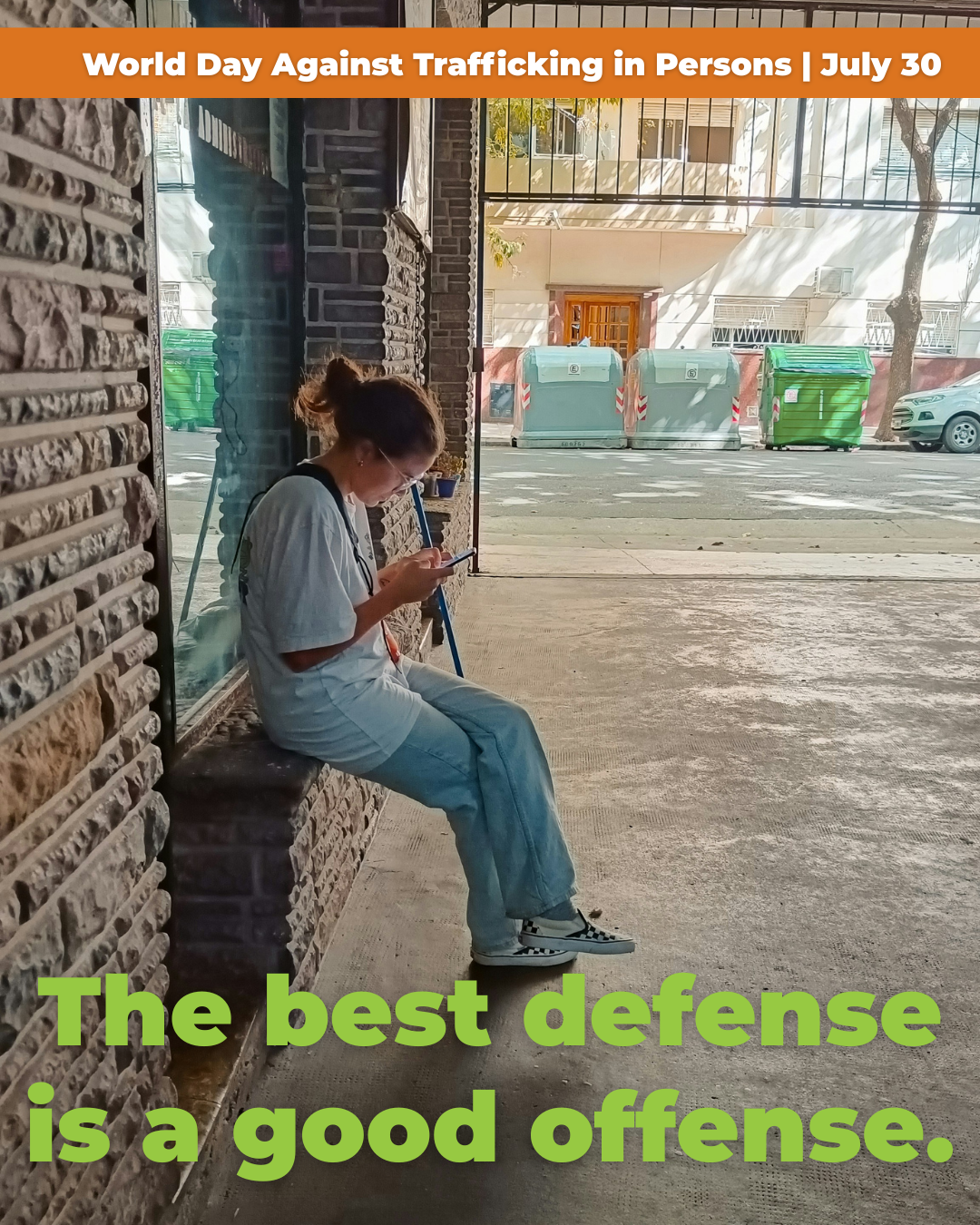A woman wearing a white shirt and light jeans sitting on a brick wall outside a building, looking at her phone. The image includes a street with parked cars and large trash bins. There is an orange banner at the top that says 'World Day Against Trafficking in Persons | July 30,' and green text at the bottom that reads, 'The best defense is a good offense.'