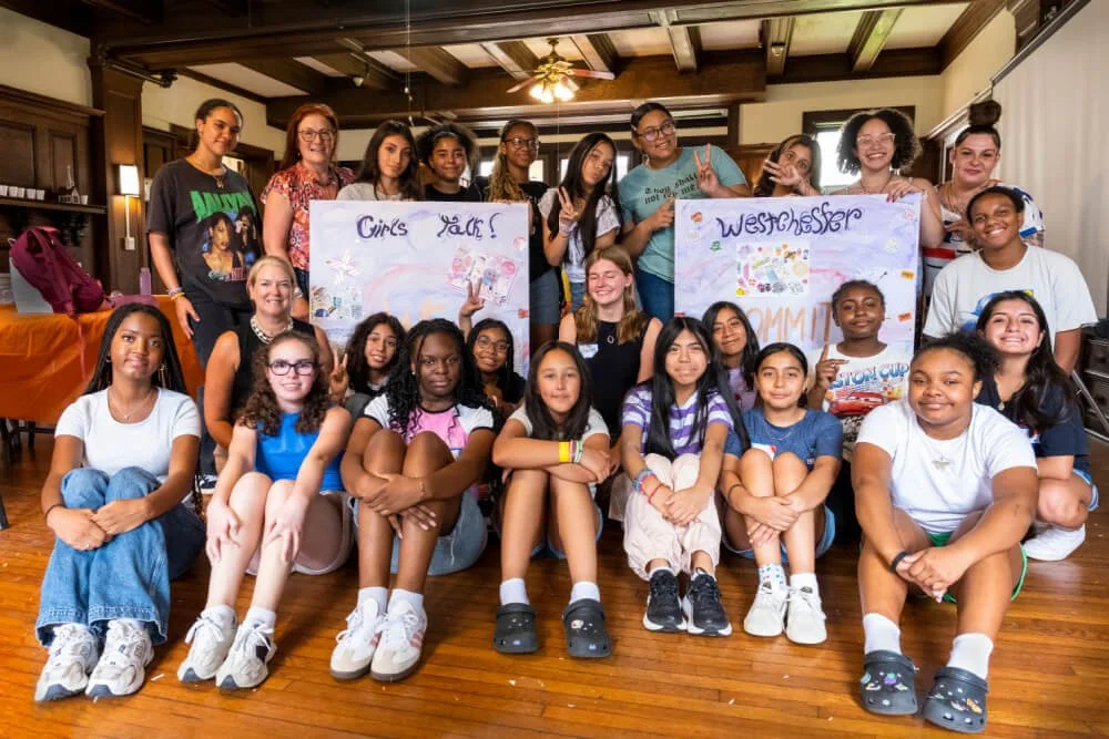 Group of diverse girls and women gathered indoors, some holding handmade posters that read 'Girls Talk!' and 'Westchester.'