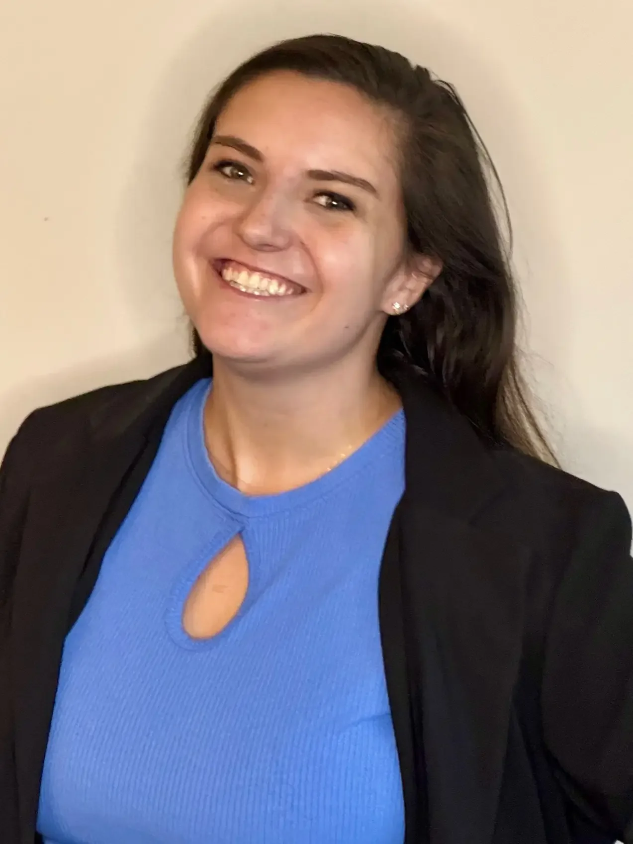 Chloe Kastner Leonardo, director of development, with long dark hair wearing a royal blue top and black blazer, standing against a plain light-colored wall.