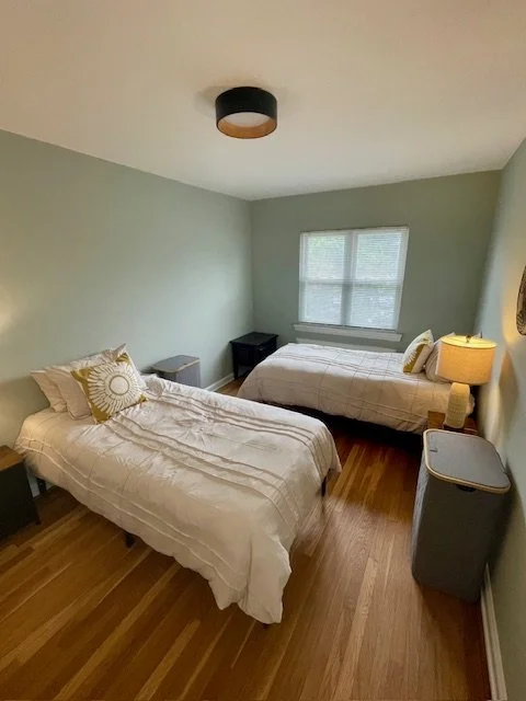 A bedroom with two twin beds, light blue walls, a window, and a floor lamp next to one bed.