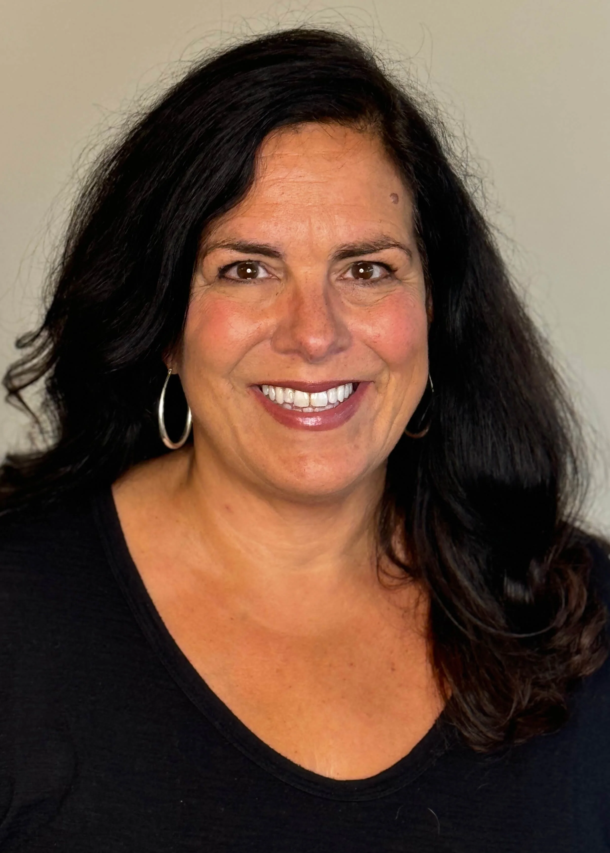 Close-up photo of Jeannie Colangelo, director of finance and technology, with curly dark hair, brown eyes, and a big smile, wearing hoop earrings and a black top.