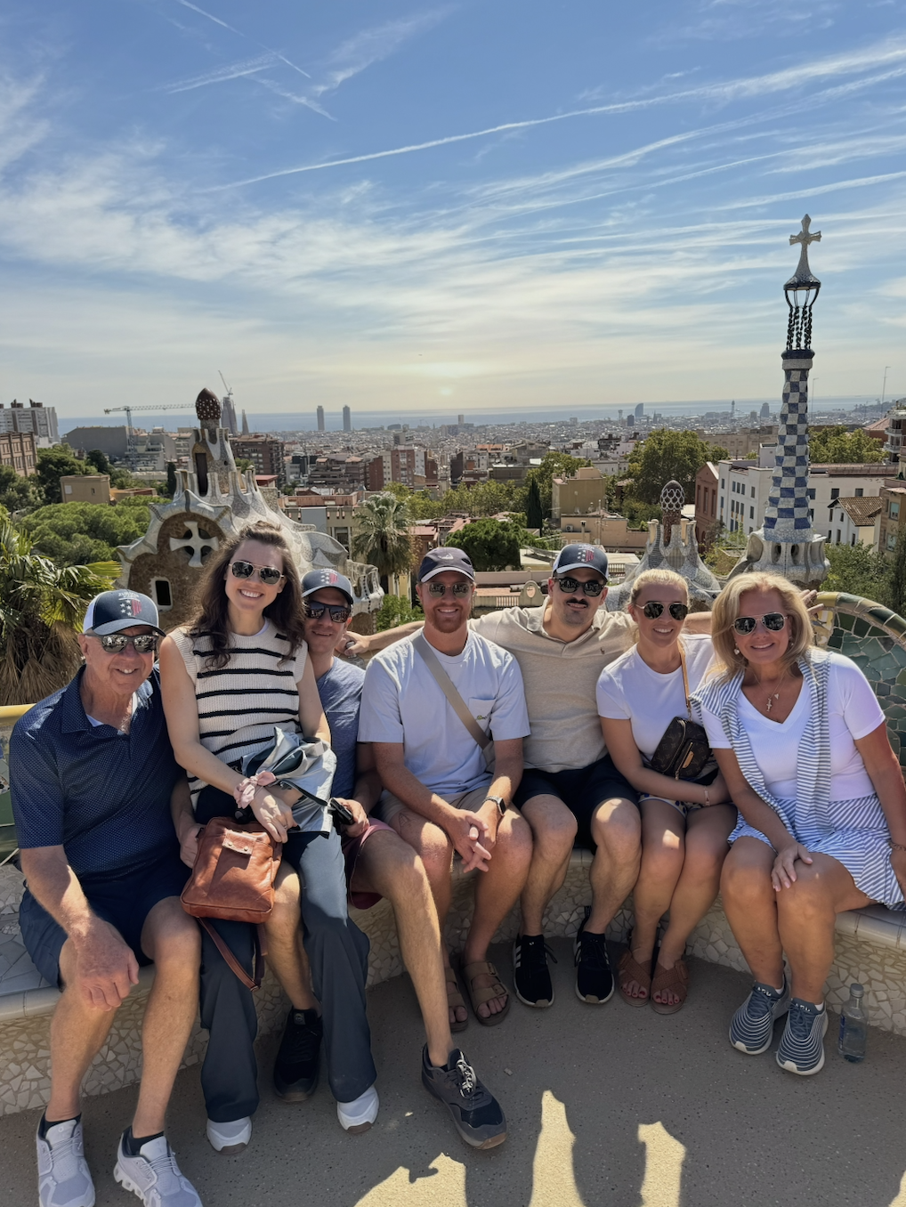 Group of people sitting on a bench in Park Güell, Barcelona, with cityscape in the background.