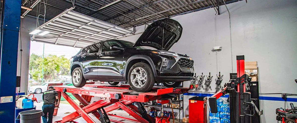 A black SUV with the hood open is lifted up high in an auto repair garage.