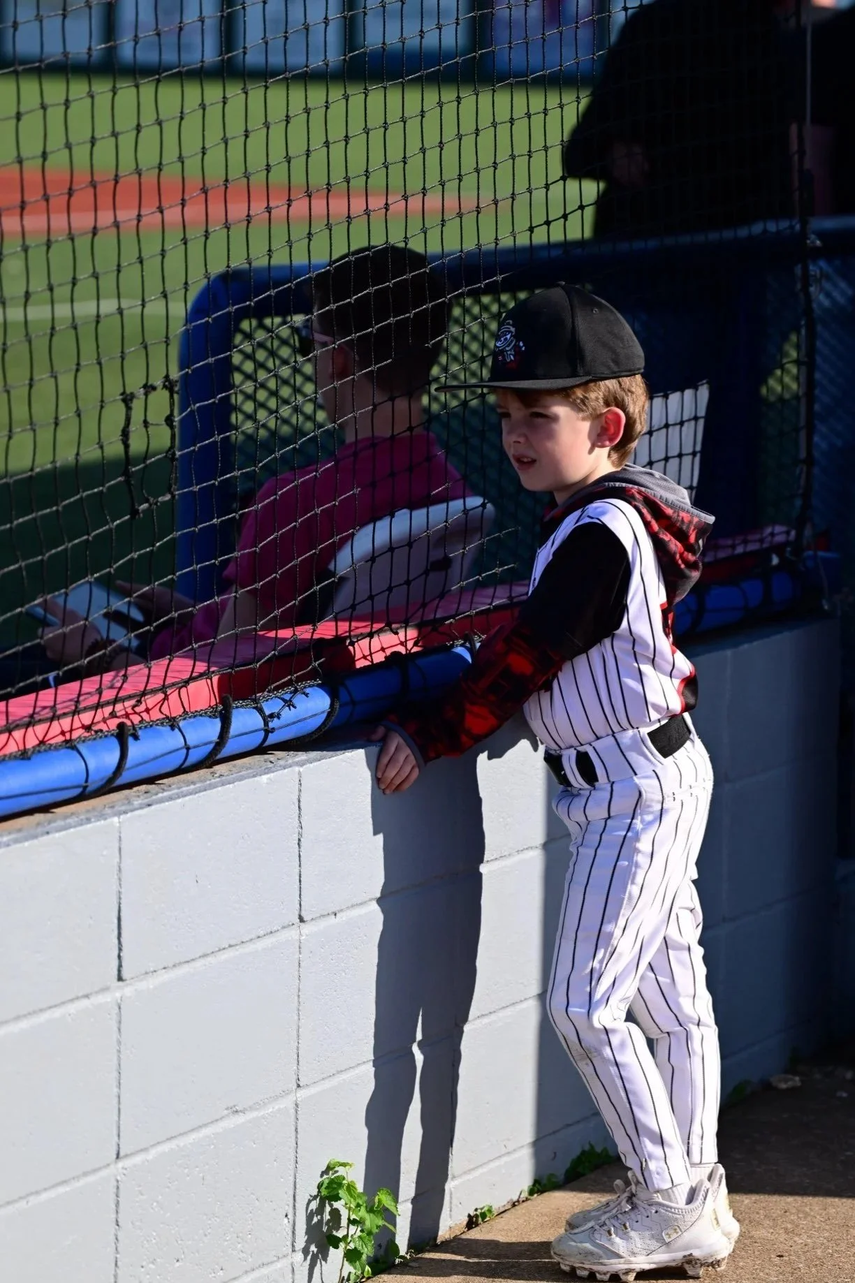 Young boy in baseball uniform by the dugout