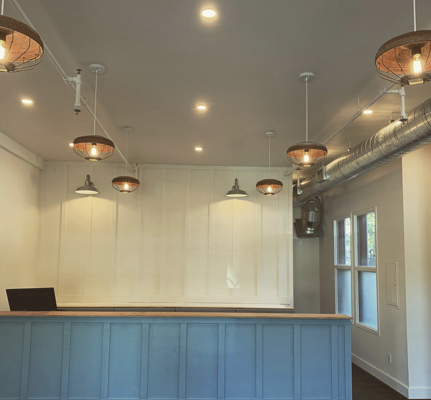 Custom outdoor kitchen lighting design featuring counter, bar and overhead lighting.  The kitchen includes a  wood-fired pizza oven, rustic wood countertops, LED lighting, and modern appliances under a wooden pergola.