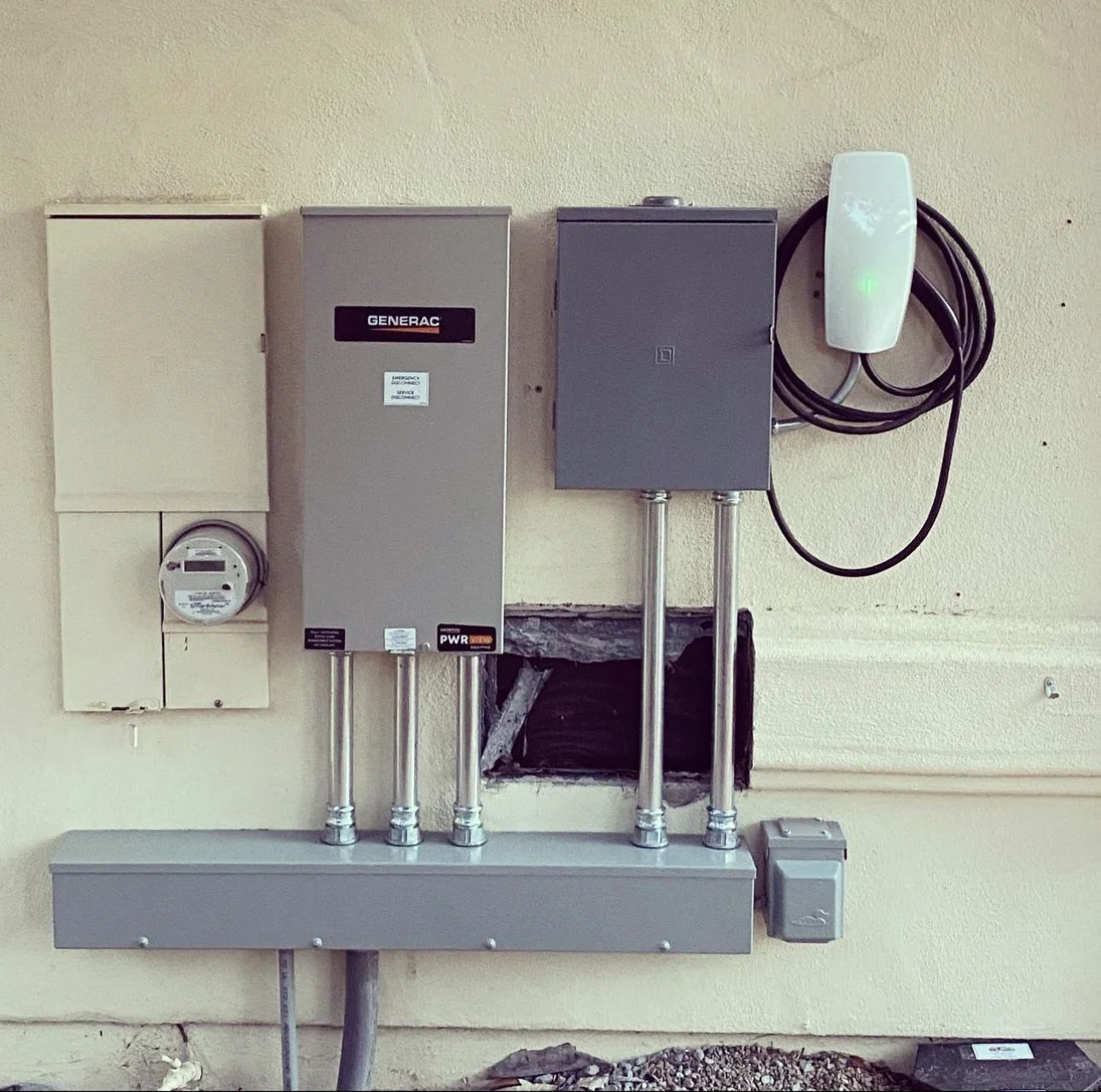 Electrical utility meter, Generac generator control panel, circuit breaker box, and an EV charging point mounted on a wall.