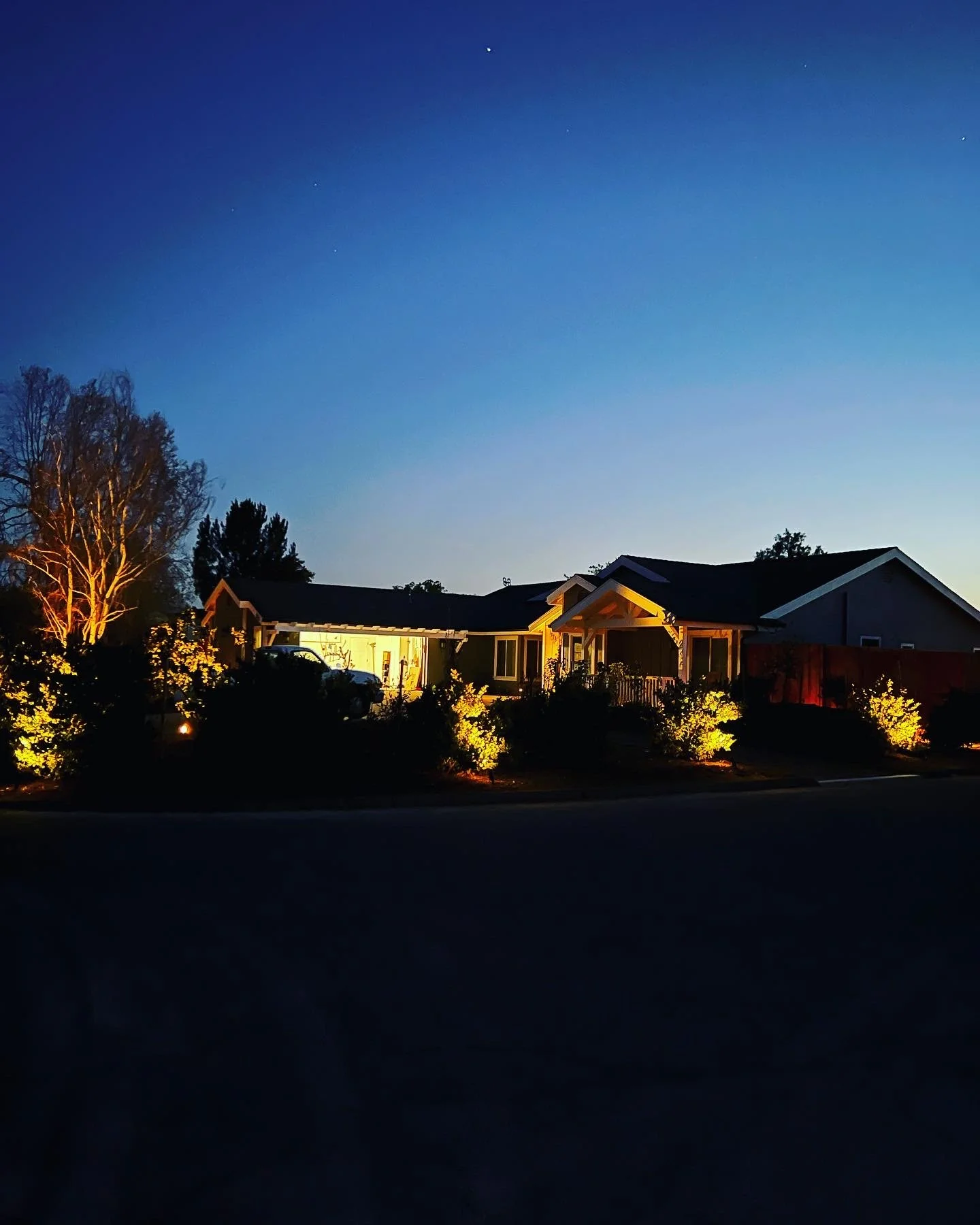House illuminated at dusk with custom landscape lighting and driveway visible.