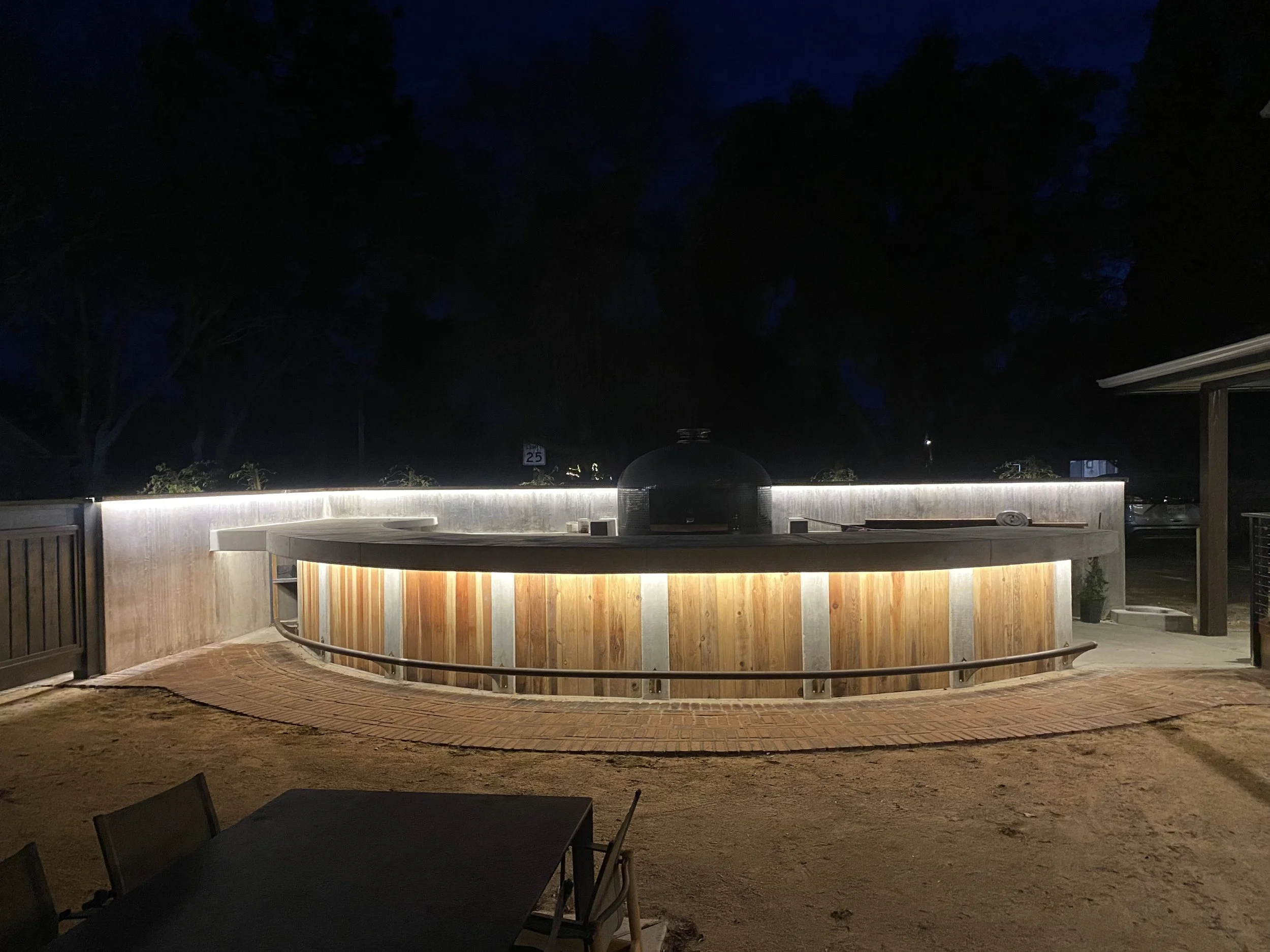 Outdoor wooden bar with custom lighting design and a pizza oven at night