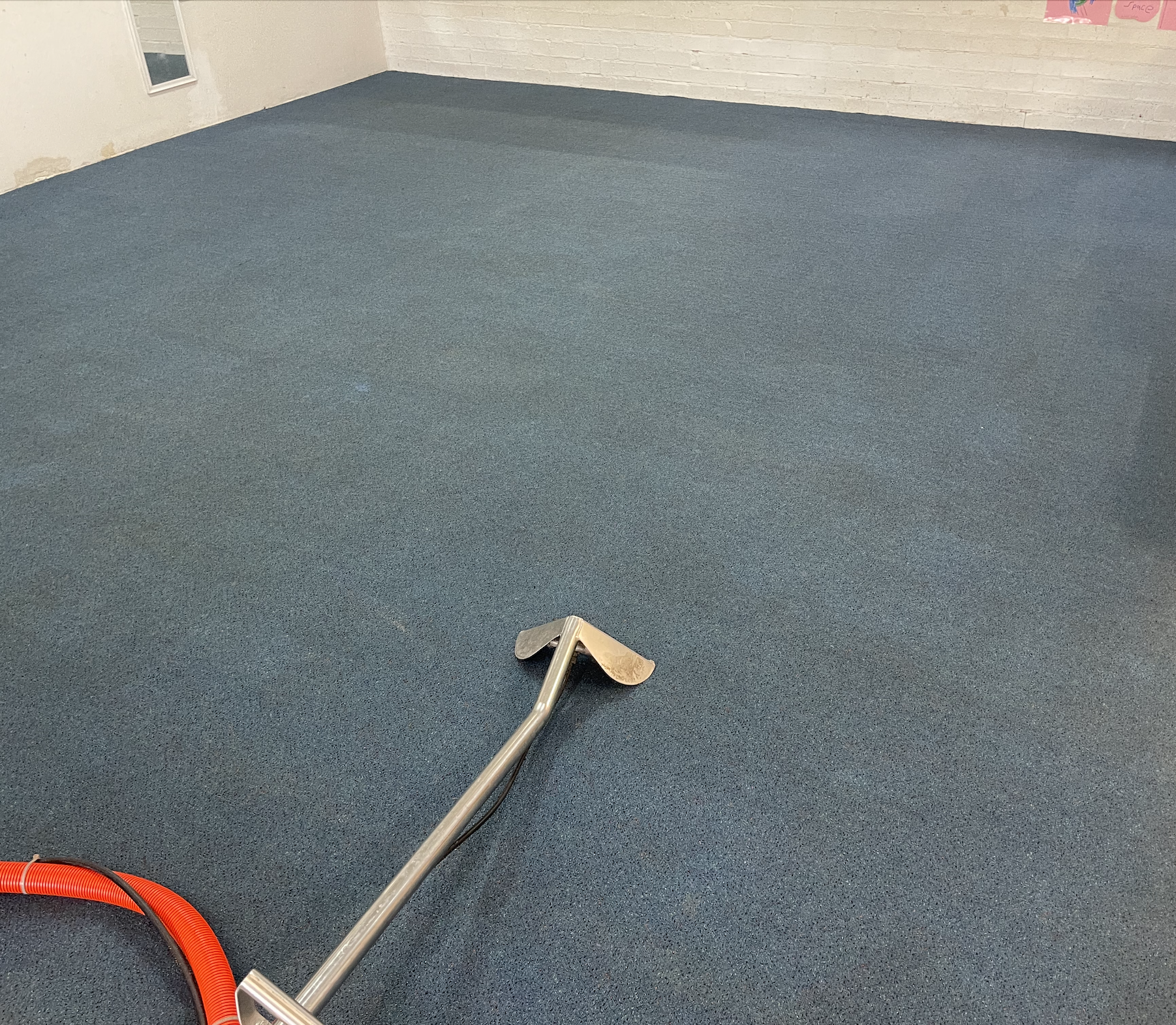 Empty room with blue carpet, white brick walls, and a red vacuum hose on the floor.