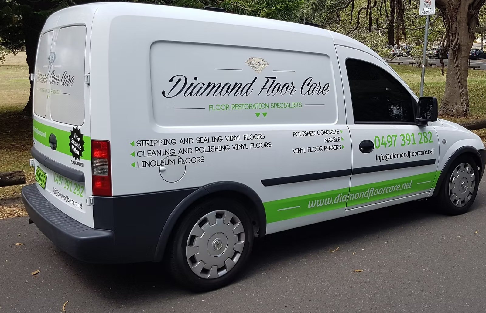 White van with green and black lettering advertising Diamond Floor Care, a floor restoration company, parked on a street with trees and a sign in the background. The van lists services such as vinyl floor stripping, sealing, cleaning, polishing, and repairs, and features the company's phone number, email, and website.