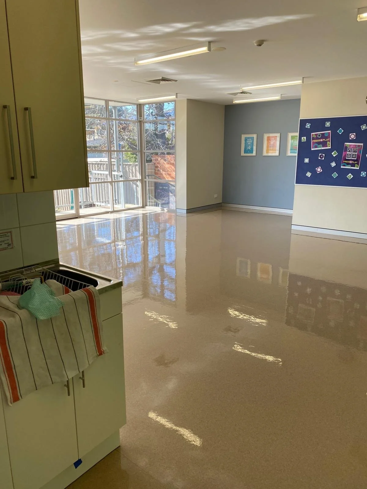 Empty classroom with large windows, colorful artwork on the walls, and a shiny tiled floor.