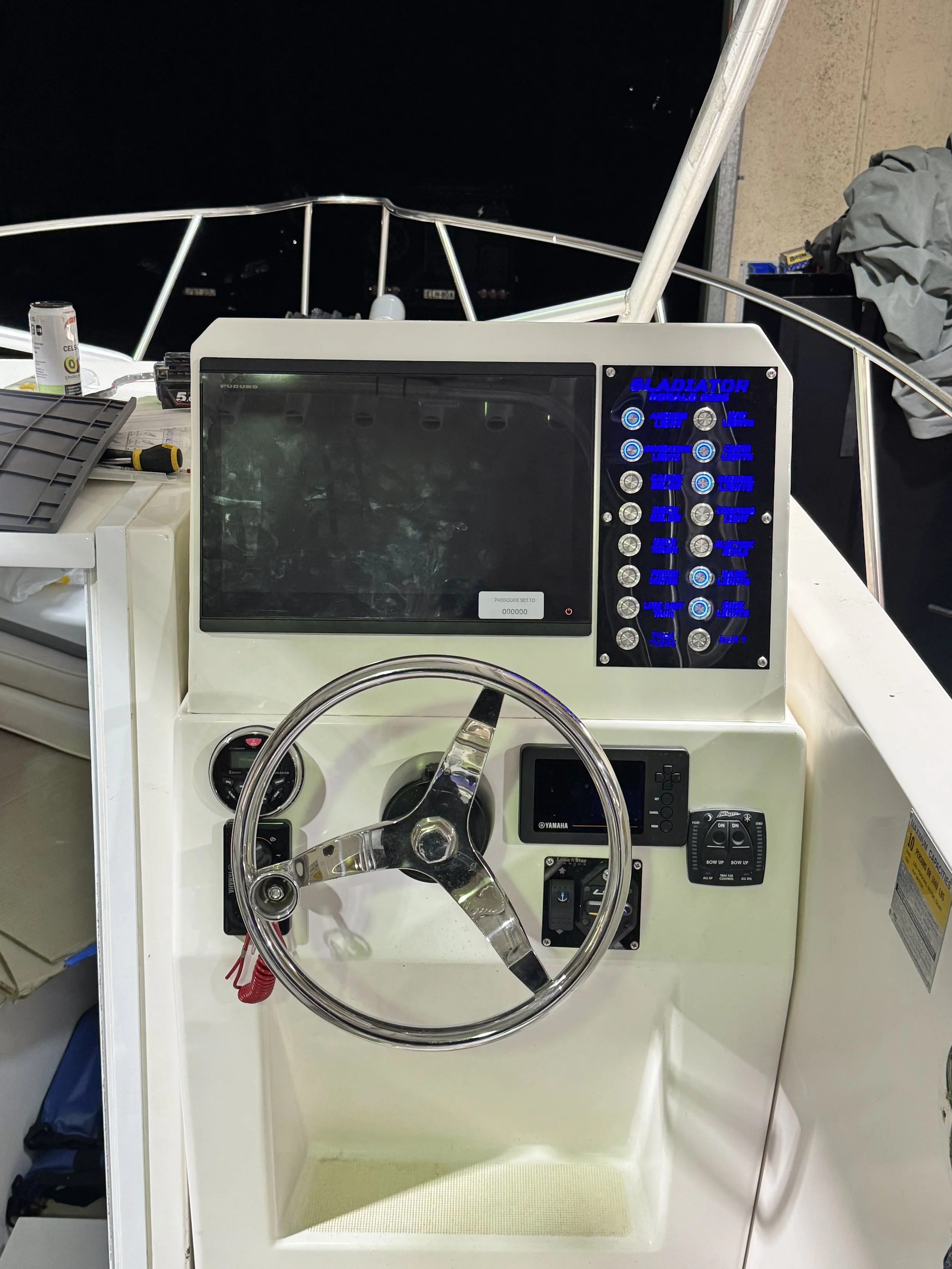 A boat helm with a steering wheel and digital display, surrounded by navigation and control buttons, on a boat at night with a dark sky