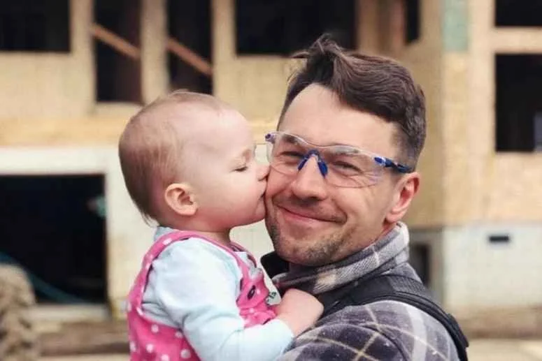 Kochubey Homes' owner with his daughter outdoors, with a partially constructed wooden building in the background.