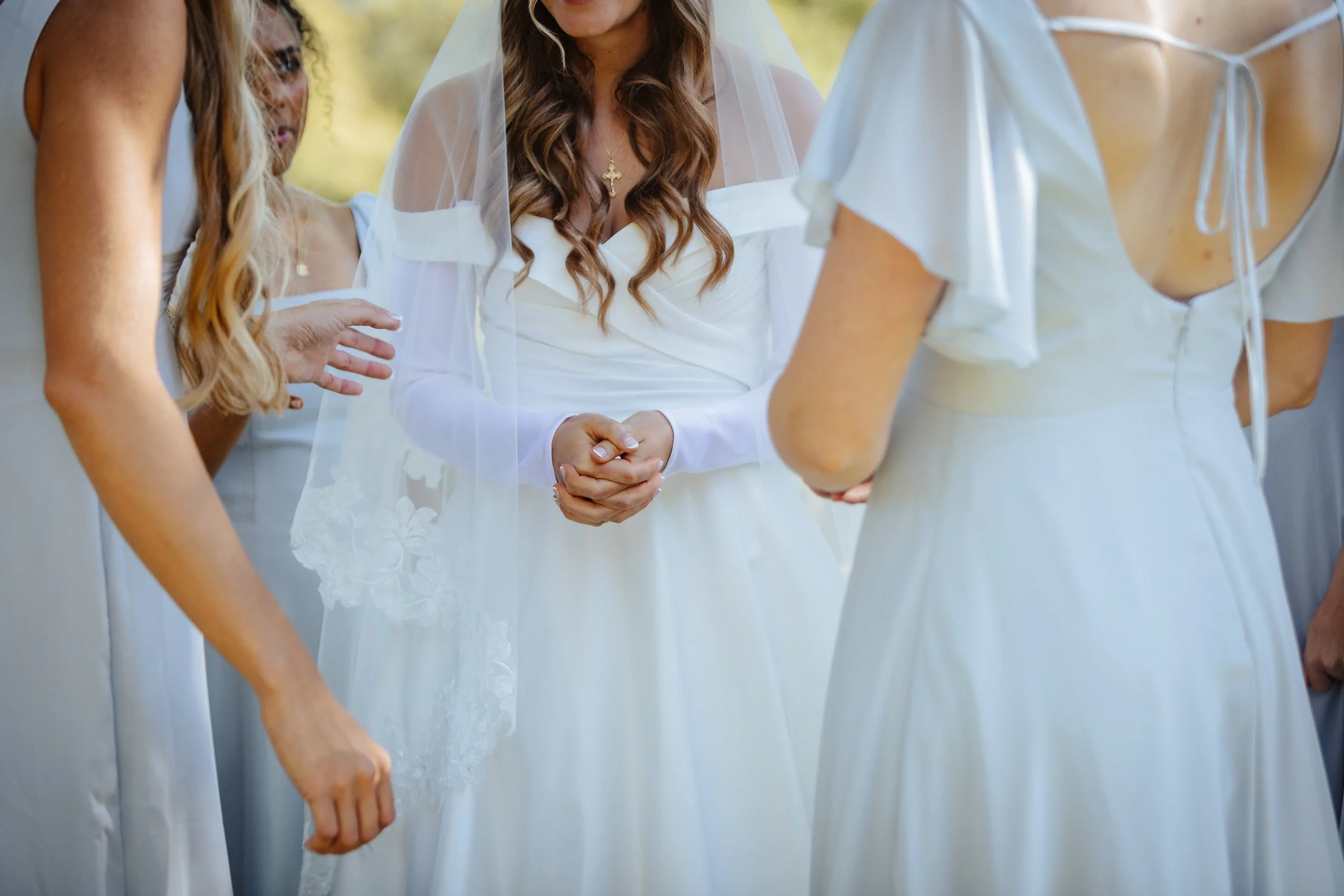 A bride in a white wedding dress and veil holding hands during a wedding ceremony, surrounded by women in white dresses.