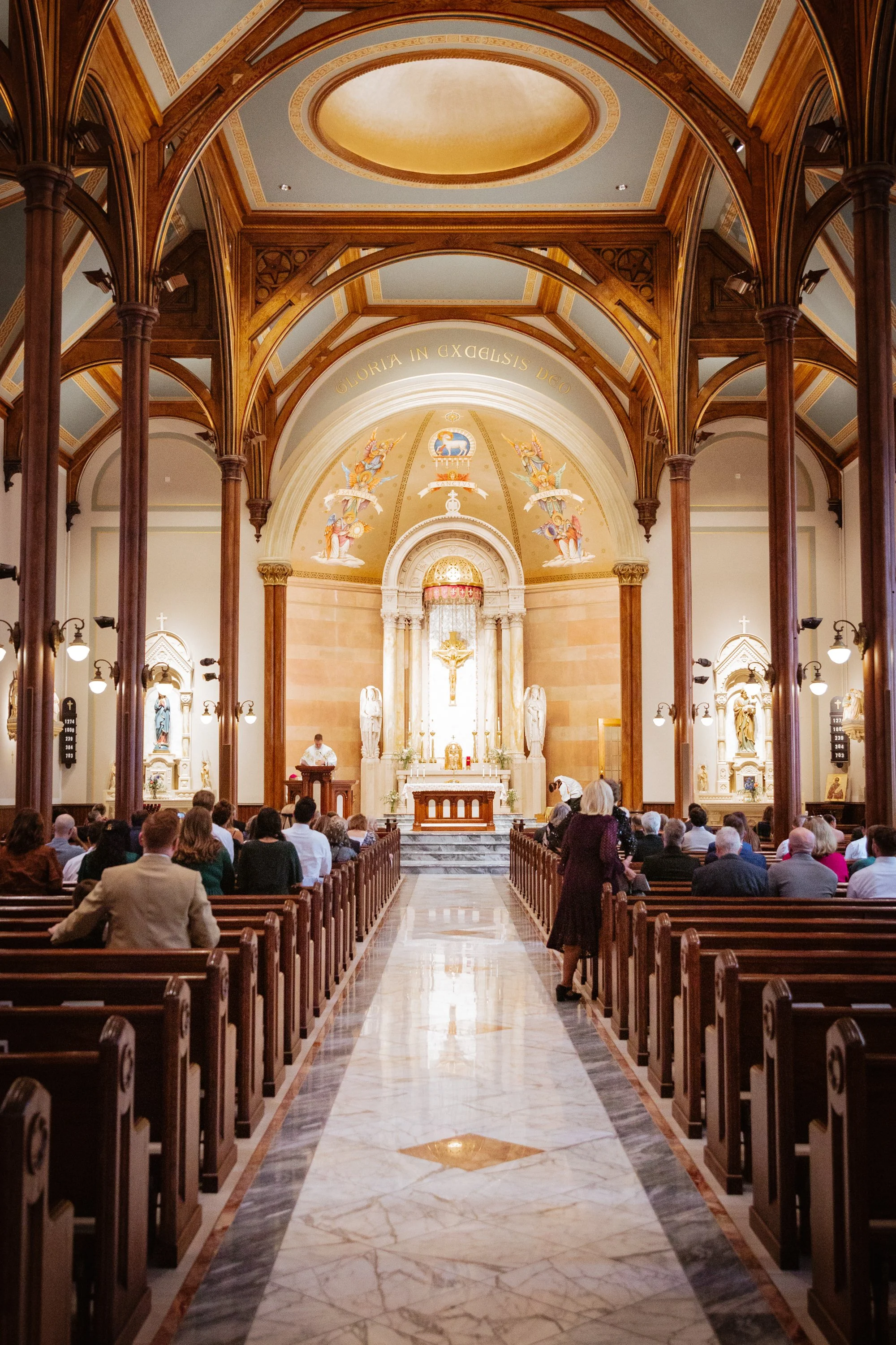 Interior of a church with wooden arches, an altar with a crucifix, and congregation seated in pews.