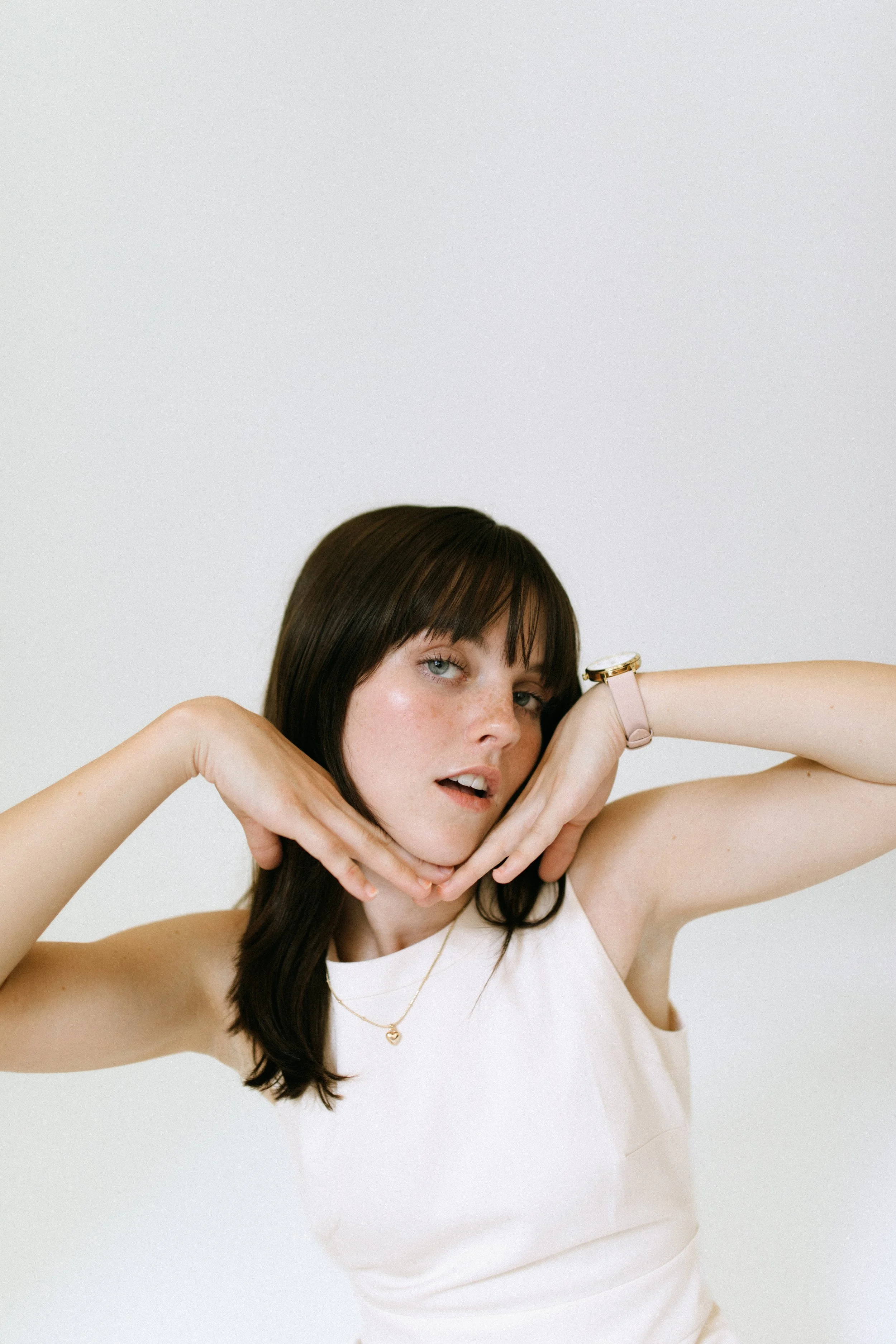 Woman posing with hands framing her face, wearing a sleeveless top and a watch.