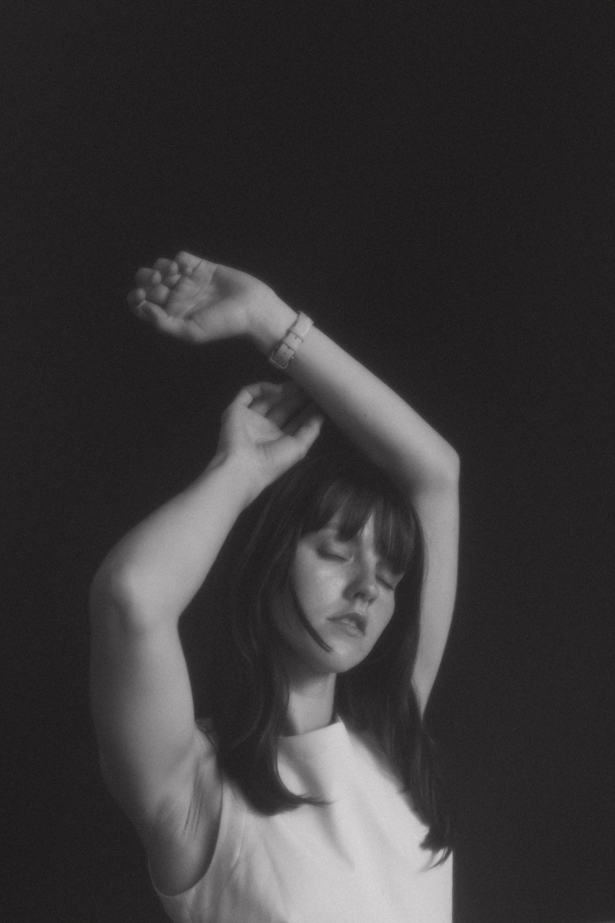 Black and white portrait of a person with arms raised, eyes closed, wearing a sleeveless top and a wristwatch.