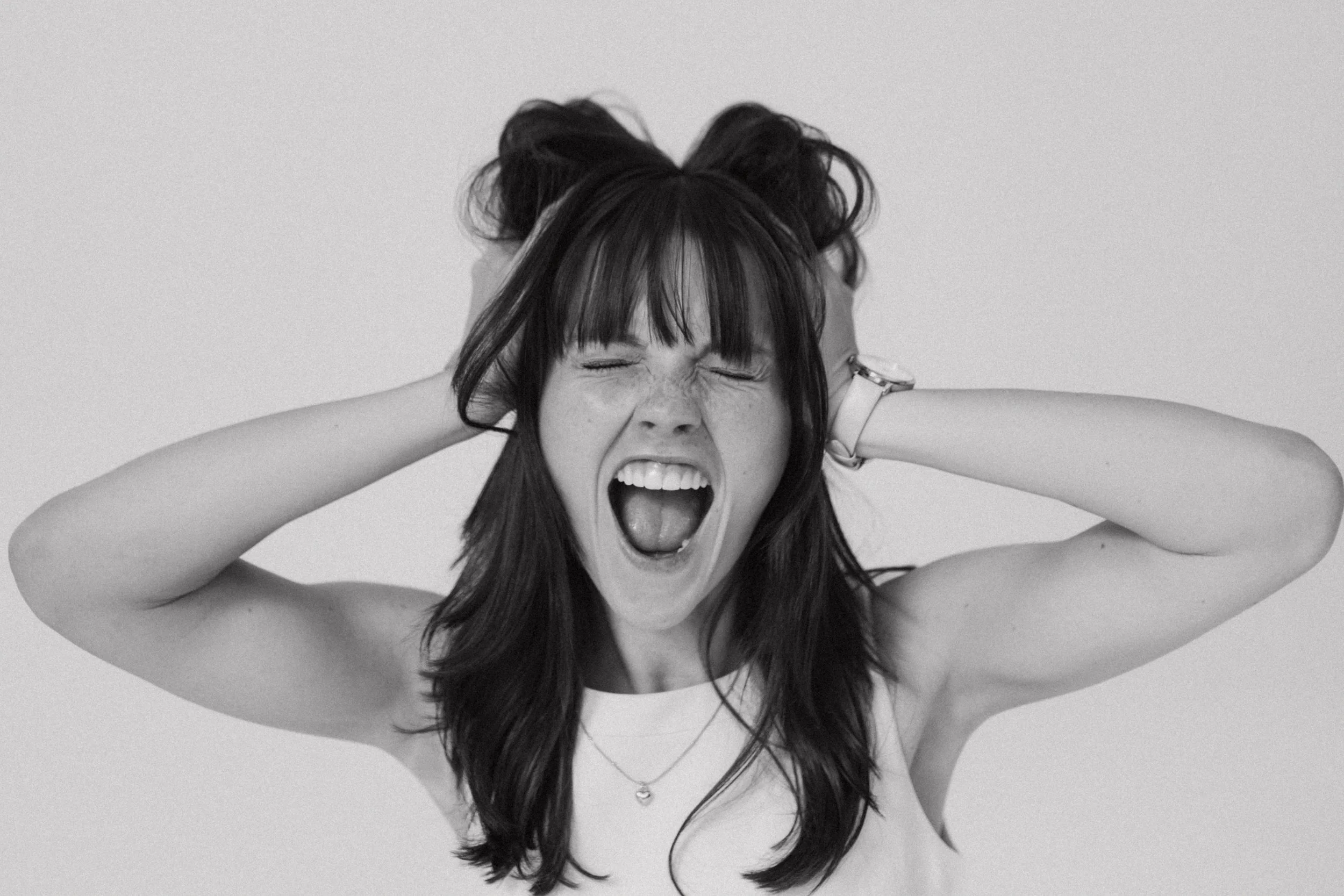 Black and white photo of a woman with long hair, expressing frustration or excitement, pulling her hair with both hands, and mouth open.