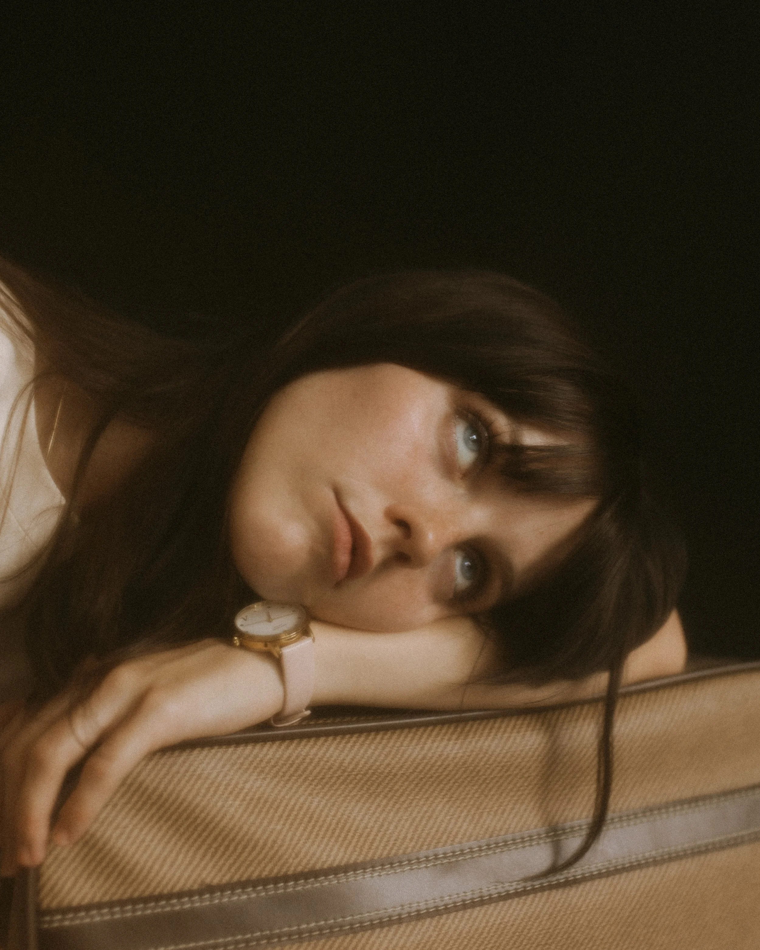 Woman with dark hair resting her head on her arm, wearing a watch, with a thoughtful expression.