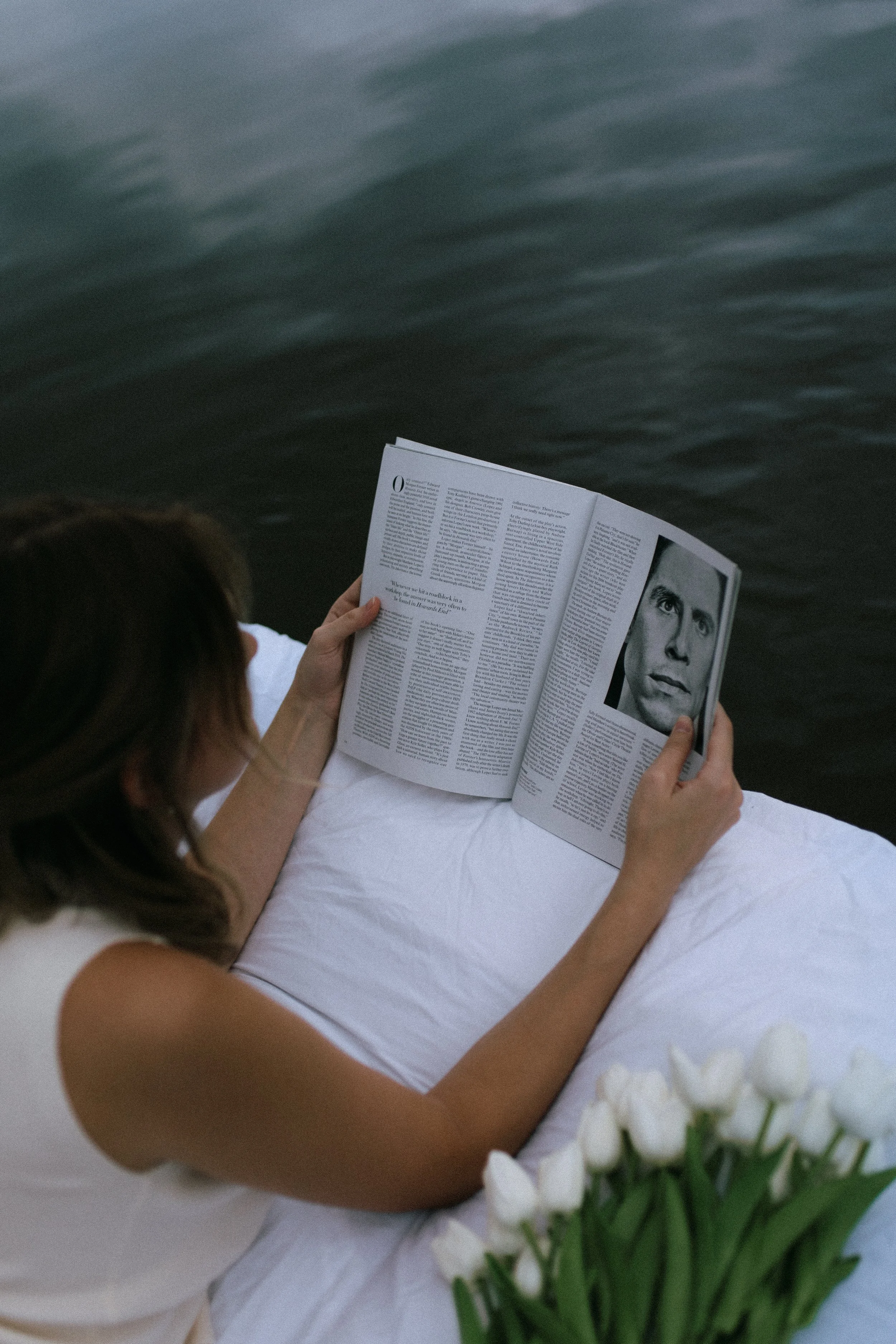Person reading magazine with portrait near water and tulips
