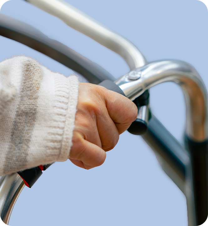 Close-up of a person's hand gripping the handlebar of a walker, wearing a beige sweater.