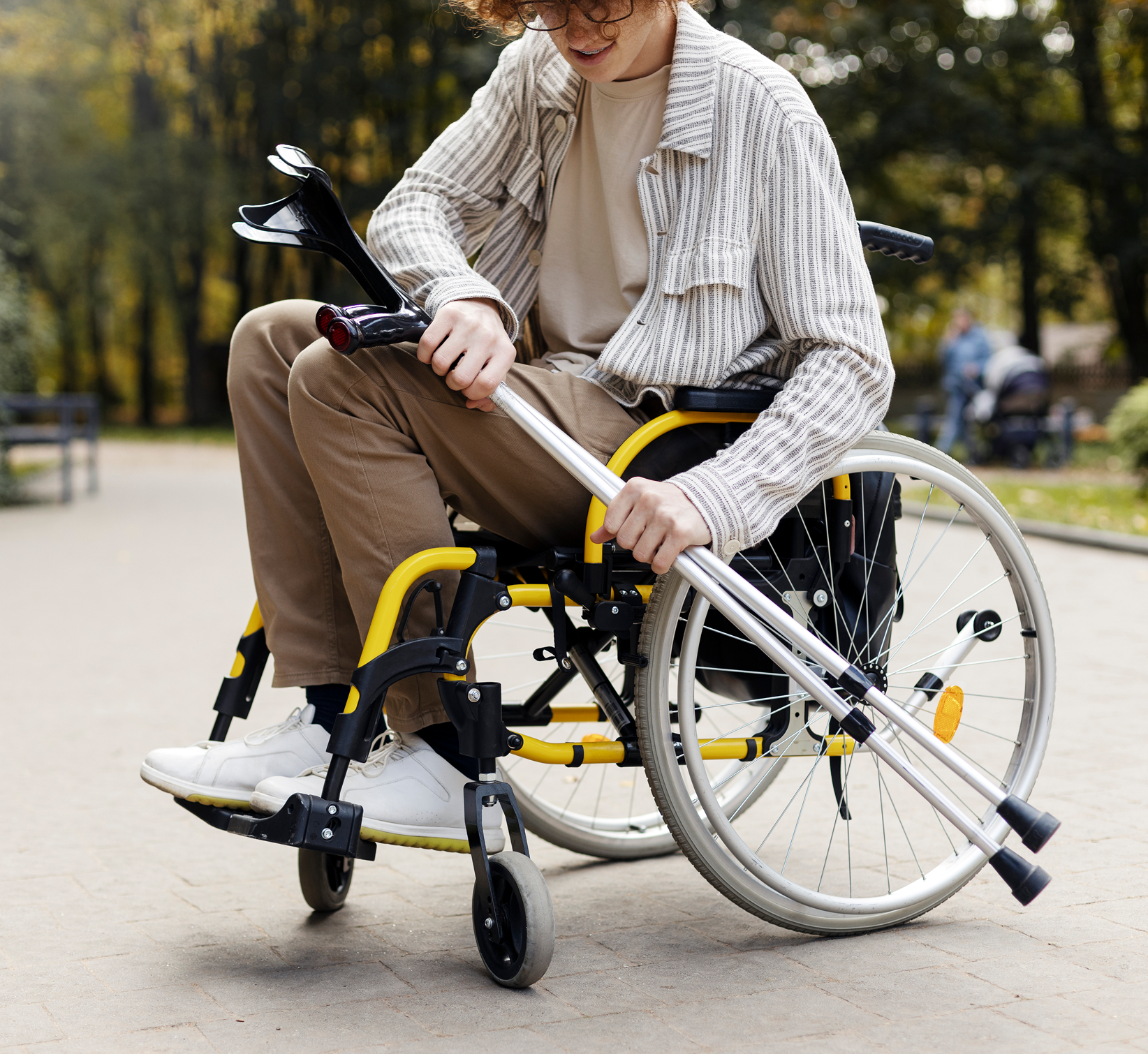 A person in a wheelchair outdoors on a sunny day, holding a crutch