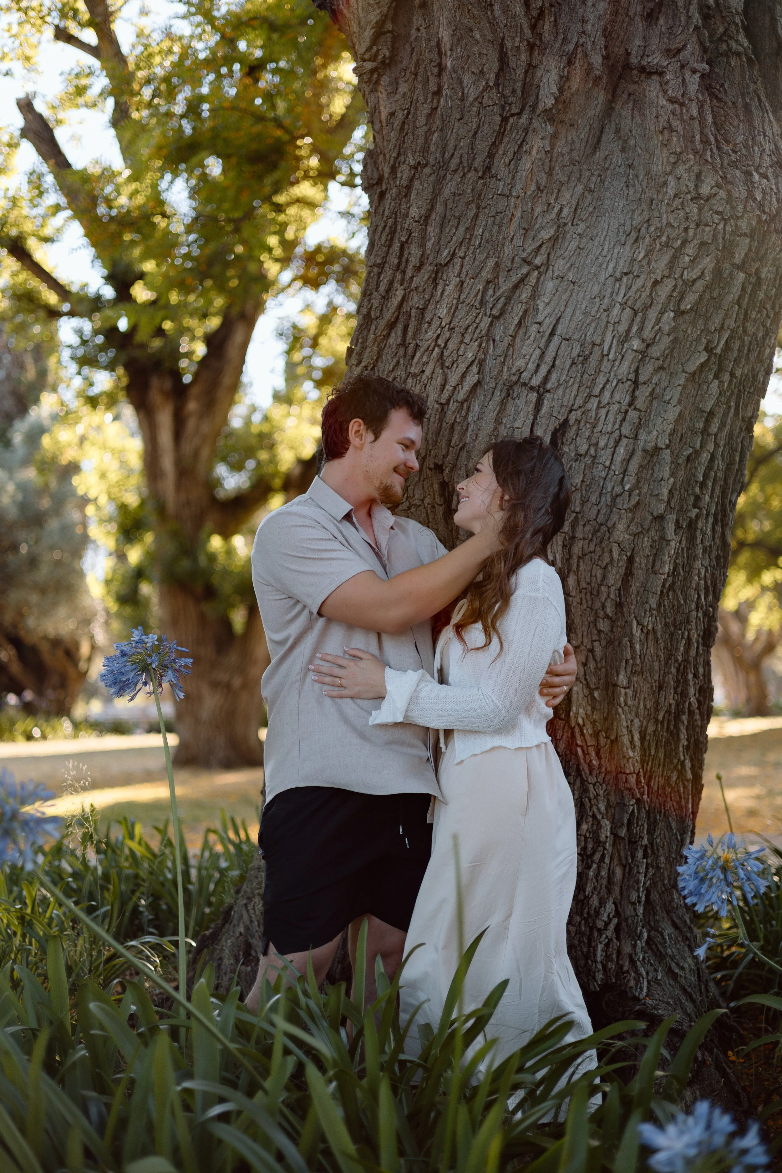 Couple embracing under a tree surrounded by blue flowers at Jardim de Belém in Lisbon