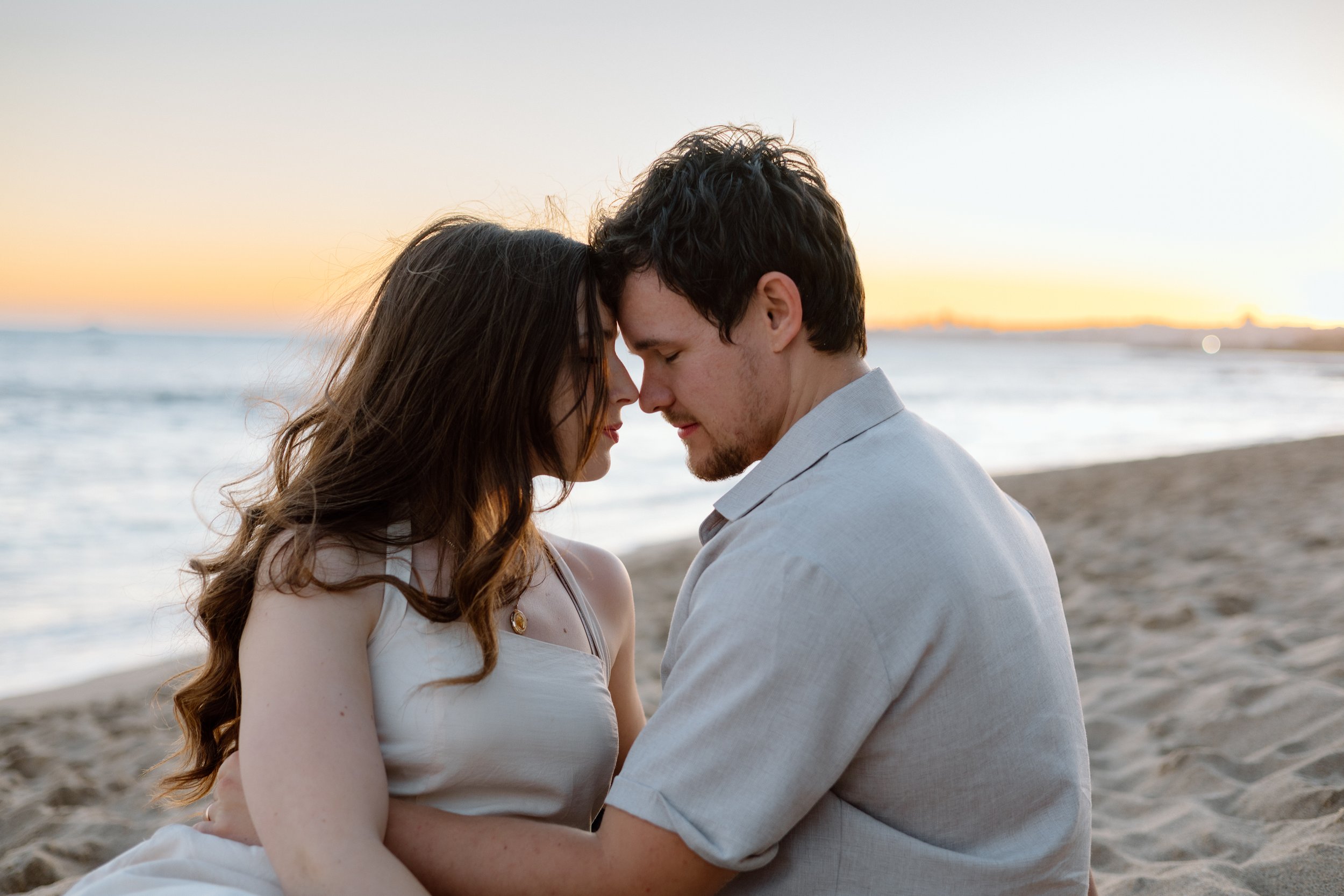 Couple sitting on the beach at sunset in Lisbon, foreheads touching, photographed by an Algarve couples photographer