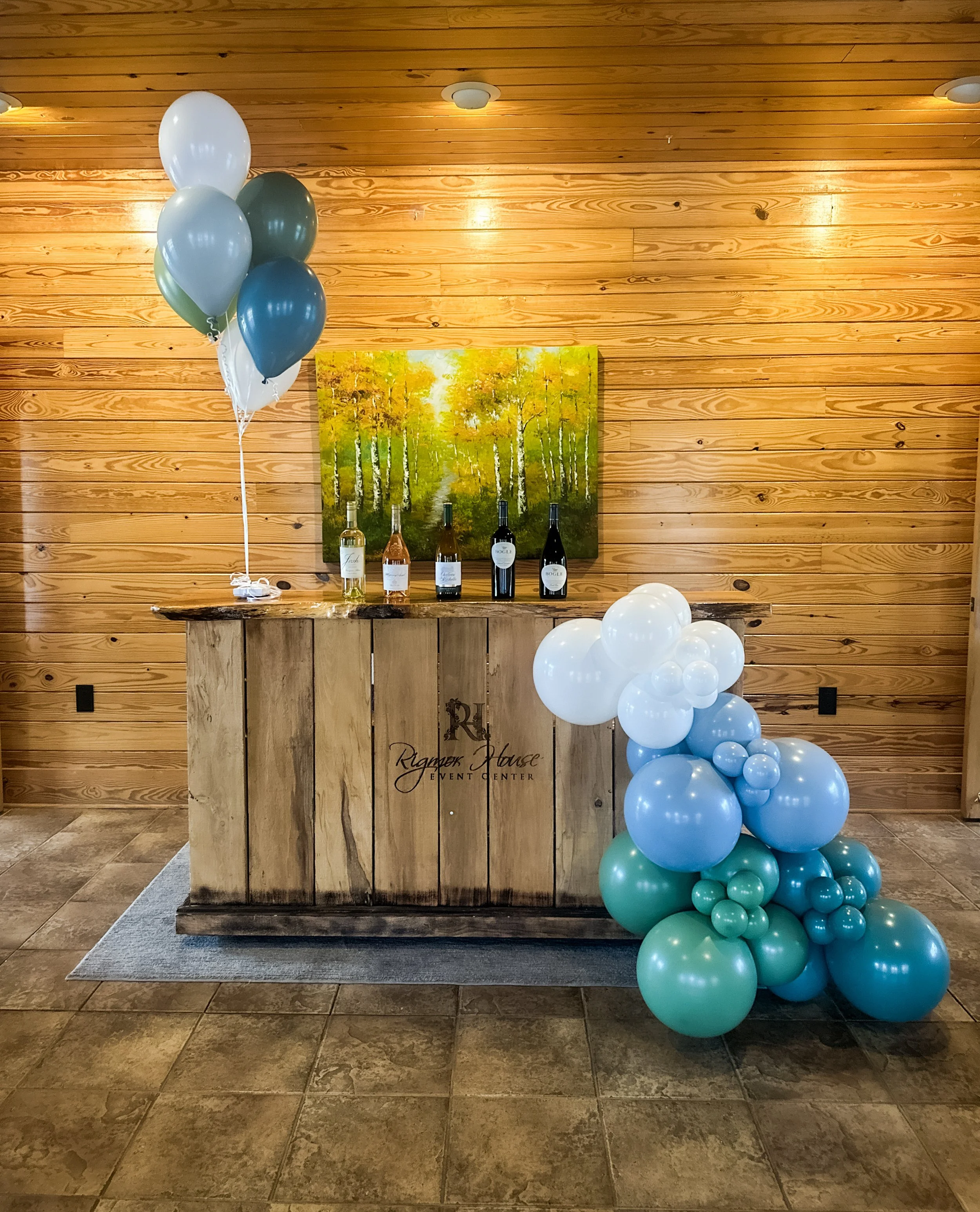 Balloon arrangement with green, blue, and white balloons next to a wooden bar at an event center