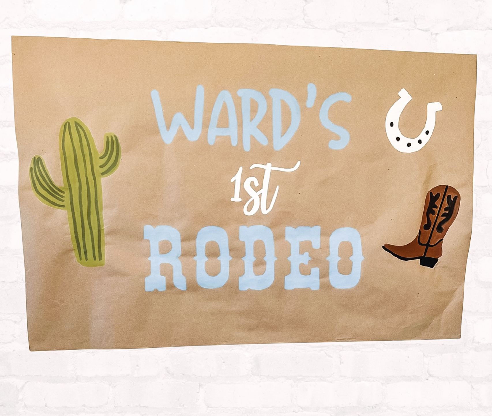 Handmade poster with text 'WARD'S 1st RODEO' surrounded by illustrations of a cactus, horseshoe, cowboy boot, and a small black dot pattern.