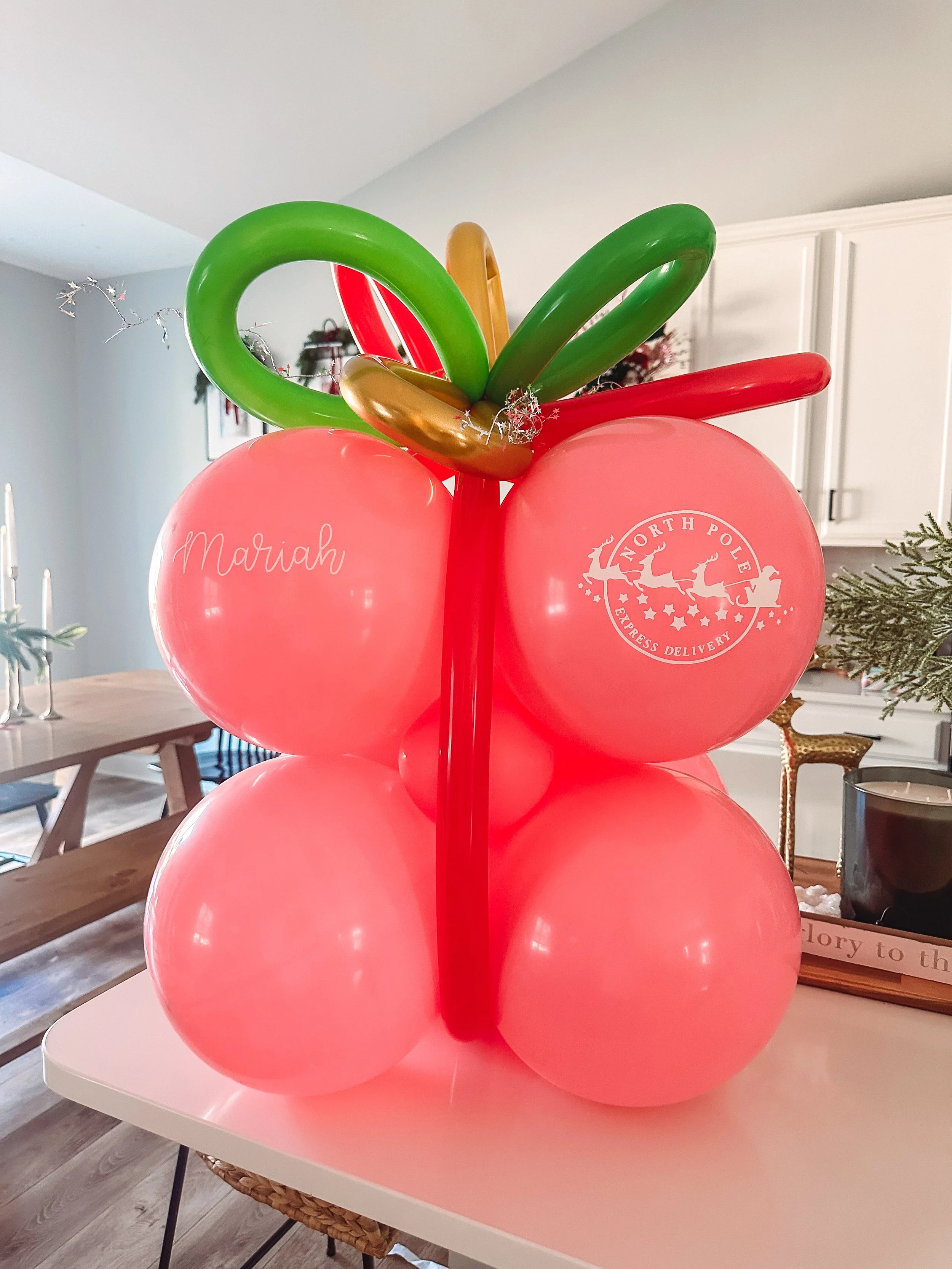 Balloon centerpiece with pink balloons and balloon decorations forming a cherry shape, featuring a personalized balloon with the name 'Mariah' and a North Pole Express Delivery logo.